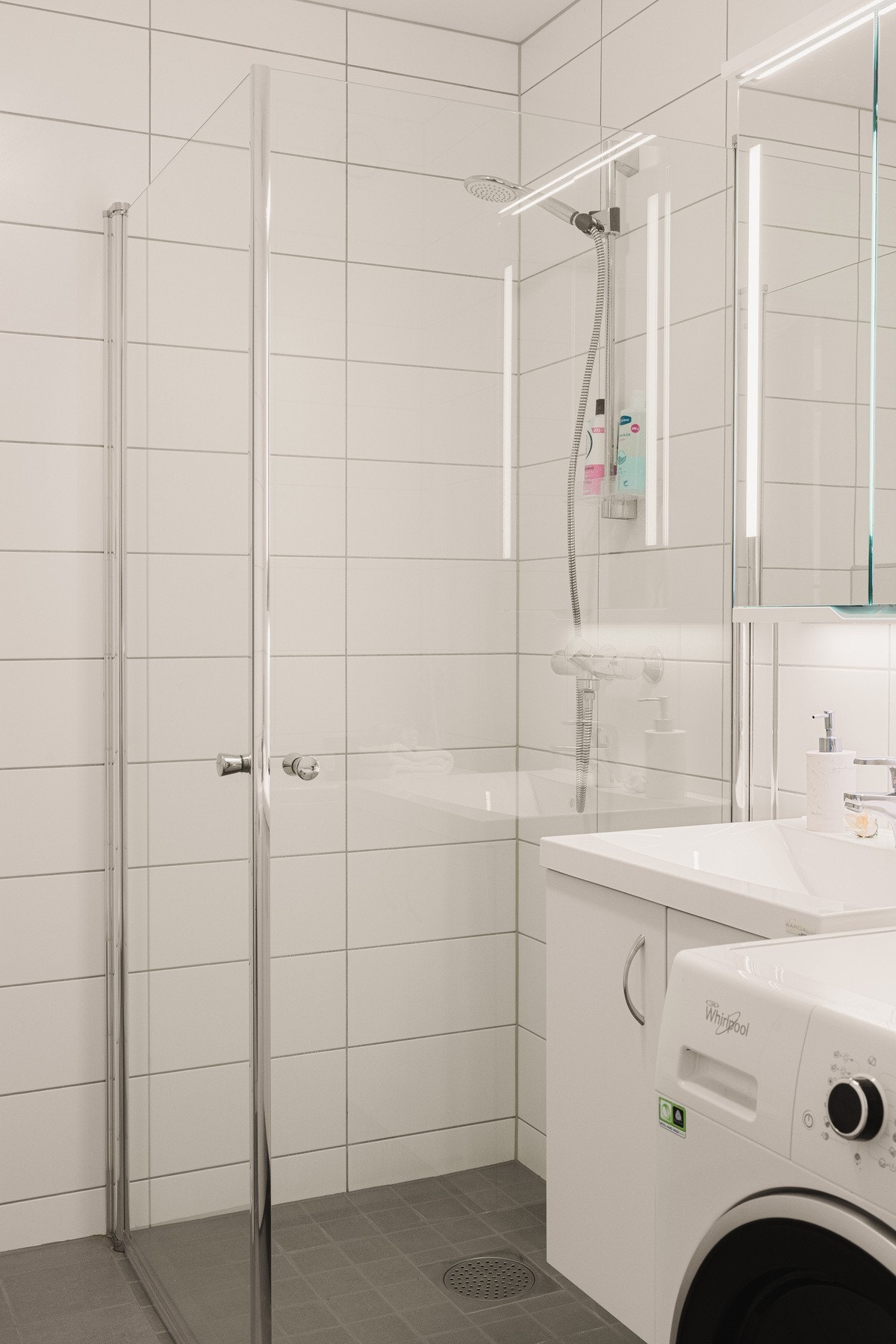 Videre er badet utstyrt med vegghengt toalett, dusjhjørne med innfellbare glassdører og opplegg for vaskemaskin. Galleribilde