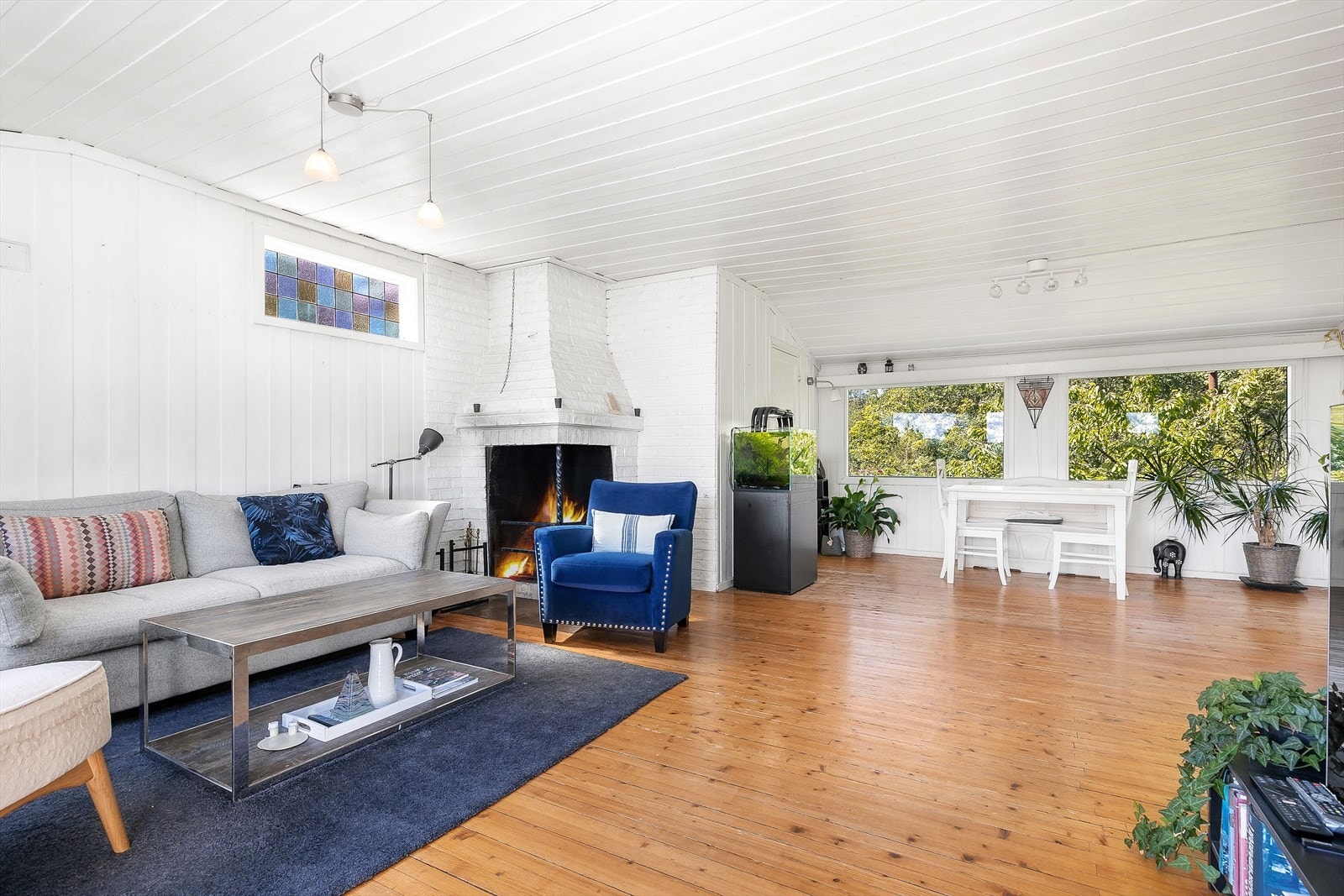 Stuen er romslig med gulvbord og malt panel på vegger, og har en elementpeis med glassdører for kjøligere kvelder. Galleribilde