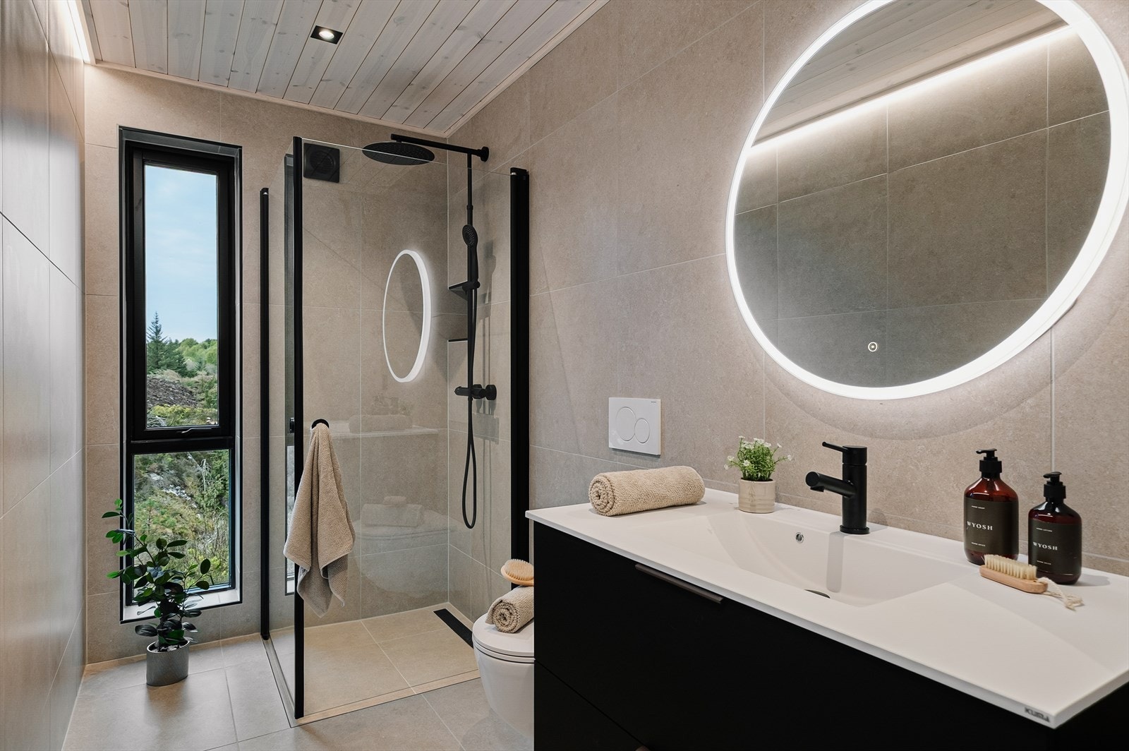 Stilrent helfliset bad, med sorte detaljer, og spotter i taket. Badet er innredet med helstøpt servant med skuffer under, led-lys speil over vask. Galleribilde