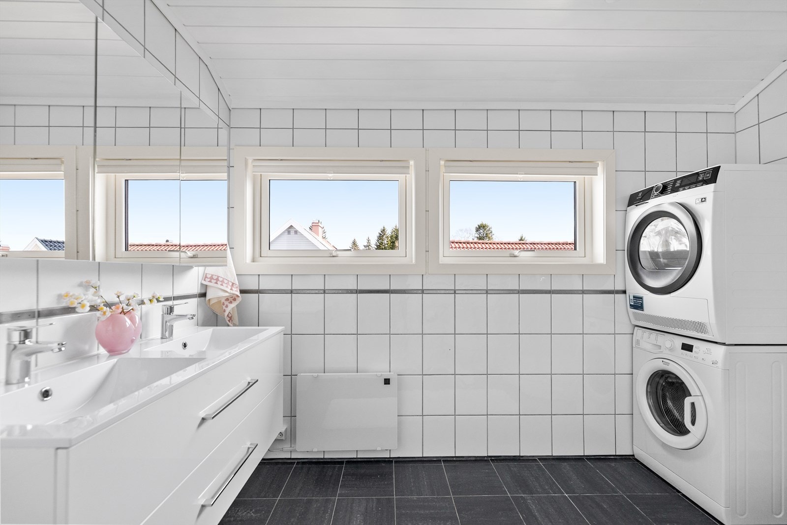 Badet fremstår som praktisk og funksjonelt utformet, med flislagt gulv og vegger som gir et tidløst og lettstelt uttrykk. Rommet er godt tilrettelagt for en travel hverdag, og byr på gode løsninger som kombinerer komfort og brukervennlighet. Galleribilde