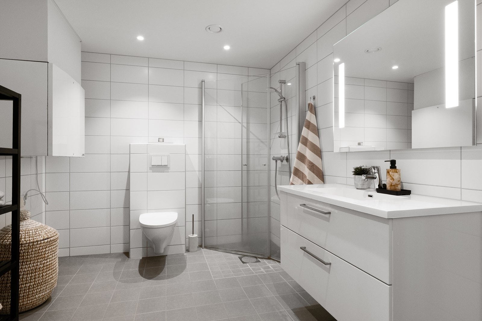 Badet er lyst og moderne, med fliser på gulv og vegger, samt malte plater i himlingen med downlights. Galleribilde