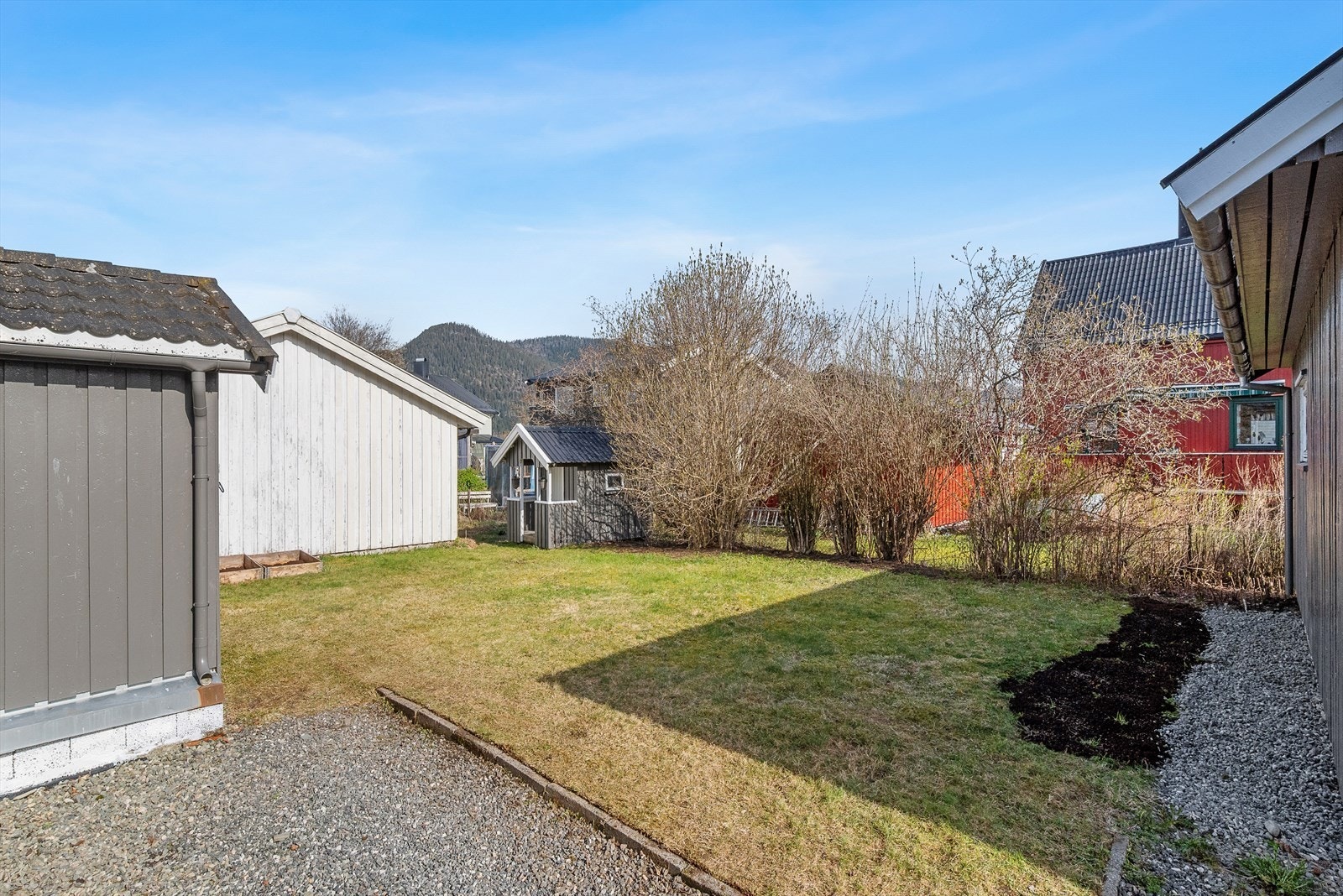 Flat tomt, opparbeidet med plen, beplantning og gruset gårdsplass. Galleribilde