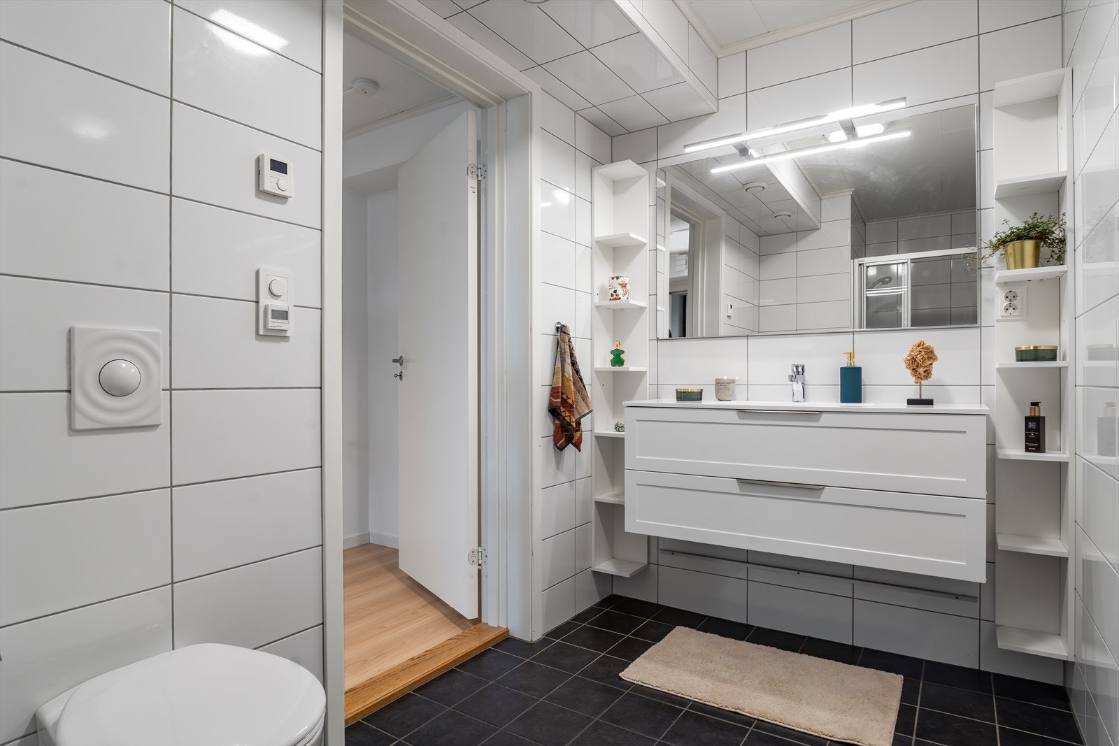 Lekkert, helfliset bad med varmekabler i gulv, mørke fliser på gulv og hvite, lyse veggfliser. Galleribilde