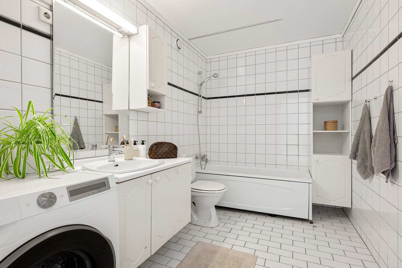 Badet er flislagt og har en praktisk utforming med badekar, servantinnredning, toalett og opplegg for vaskemaskin. Galleribilde