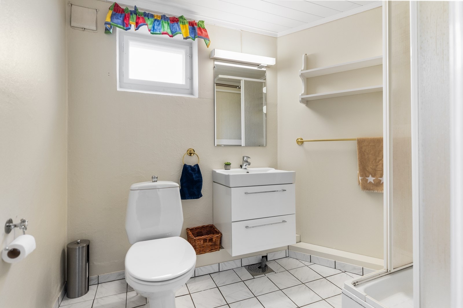 Badet i underetasjen fremstår som funksjonelt innredet med fliser på gulvet og elektriske varmekabler i deler av gulvet, som gir økt komfort. Veggene er kledd med malt tapet, og taket har MDF-panel som gir et lunt og helhetlig uttrykk. Galleribilde
