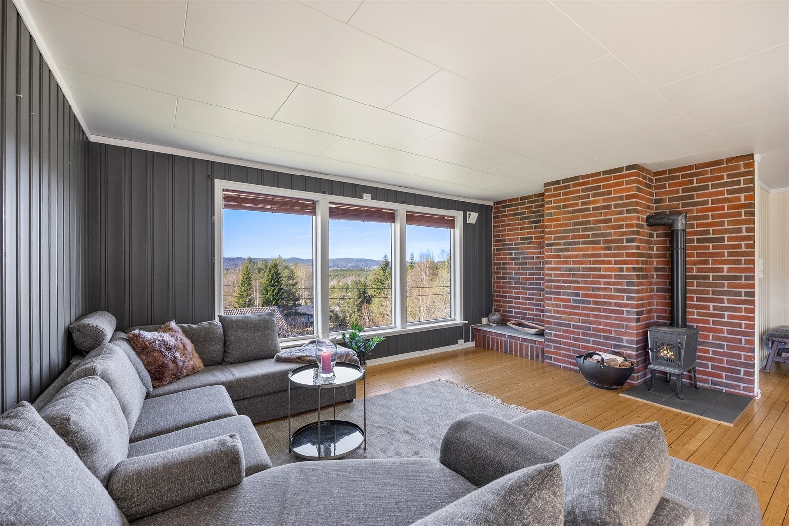 Veggen bak ildstedet er kledd i teglstein, og stuen har heltregulv i kombinasjon med hvite og mørkegrå panelvegger. Galleribilde