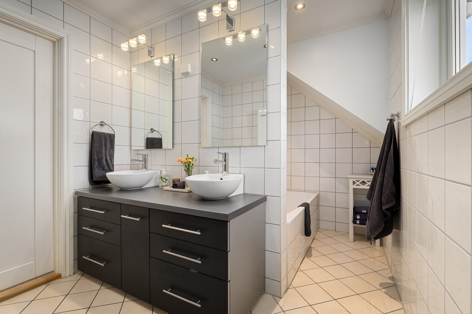 Badet har flislagte overflater og gulv med varmekabler.
Badet er utstyrt med vegghengt toalett, dobbel servant, dusjhjørne og badekar. Galleribilde