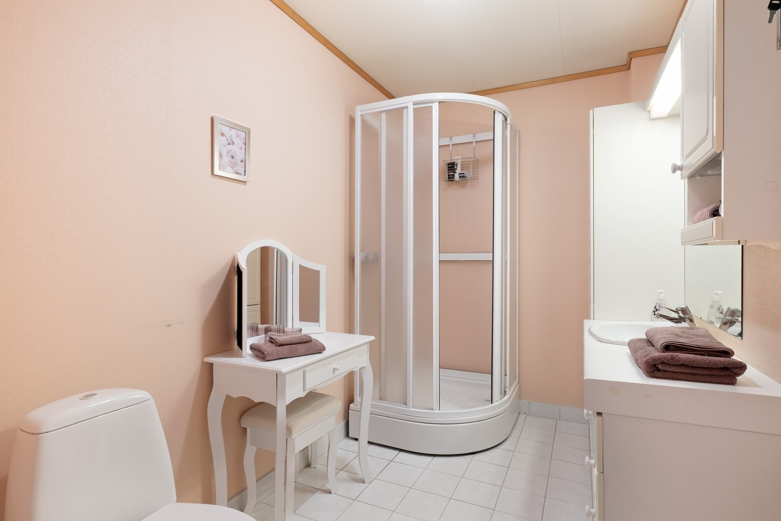 Badet har malt tapet/strie på veggar og flis på golv. Badet inneheld golvmontert wc, dusjkabinett, servant med underskap og skap. Galleribilde