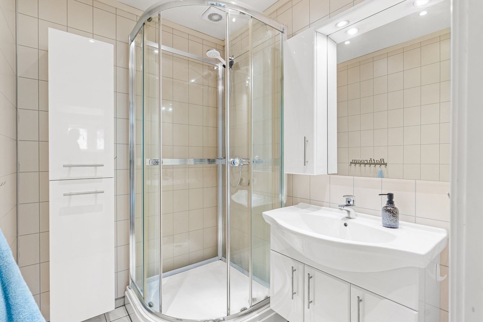 På badet er det dusjkabinett, og baderomsinnredningen består av et hvitt servantskap, et matchende veggskap, et høyskap i samme stil og et speil med belysning over servanten. Galleribilde