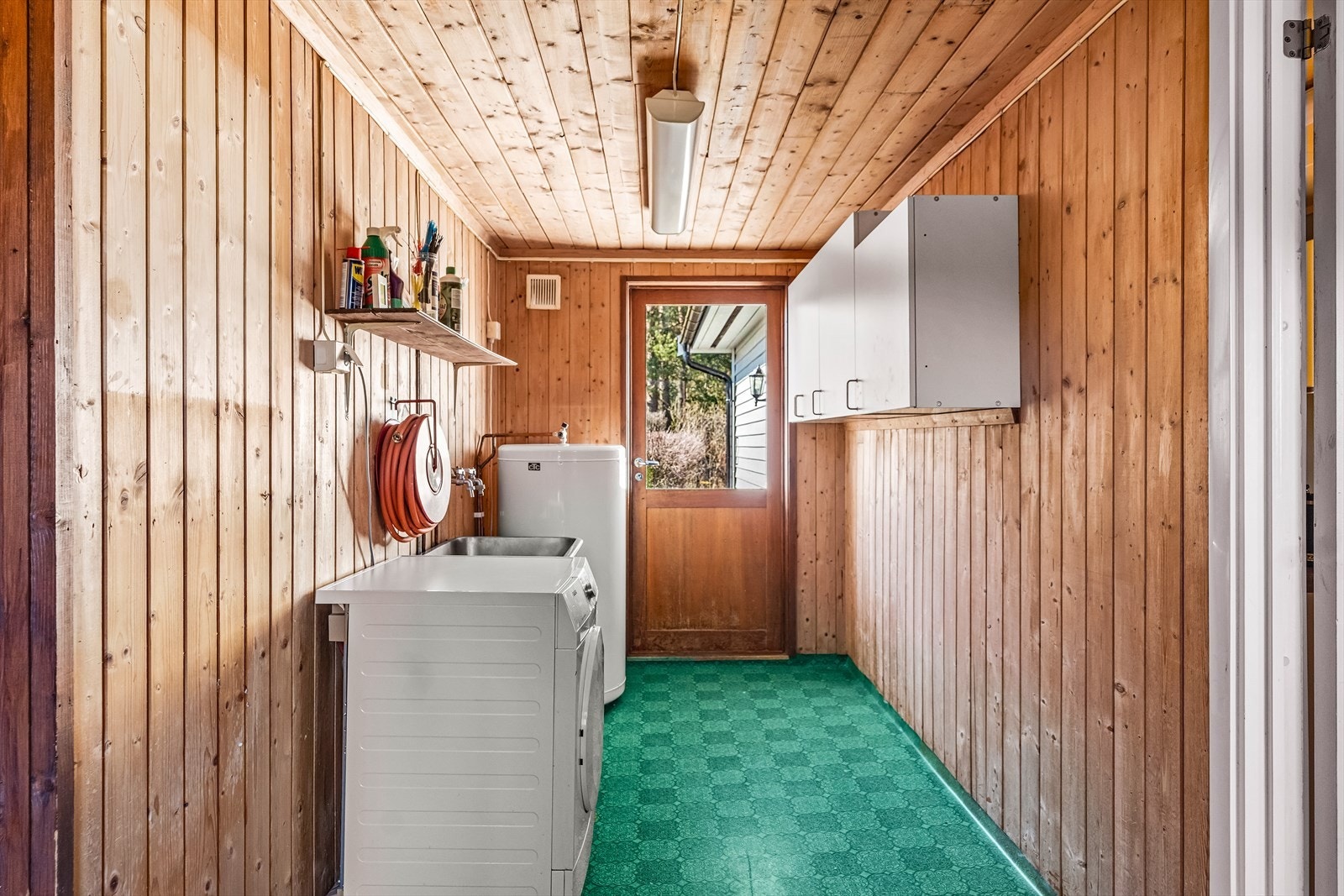Vaskerommet har glassdører ut til både inngangspartiet og hagen på fremsiden av huset. Her er det gulvbelegg, utslagsvask og veggskap med hvite fronter. Galleribilde