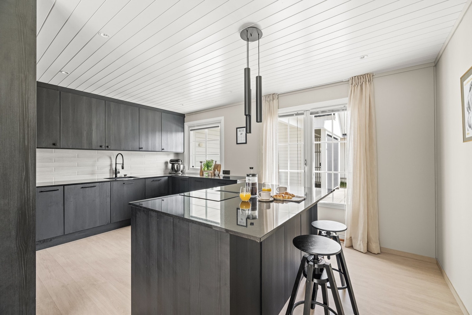 Dette er et stilrent og moderne kjøkken med mørke, glatte fronter og innredning helt opp til taket, som gir både et eksklusivt uttrykk og masse oppbevaringsplass. Galleribilde