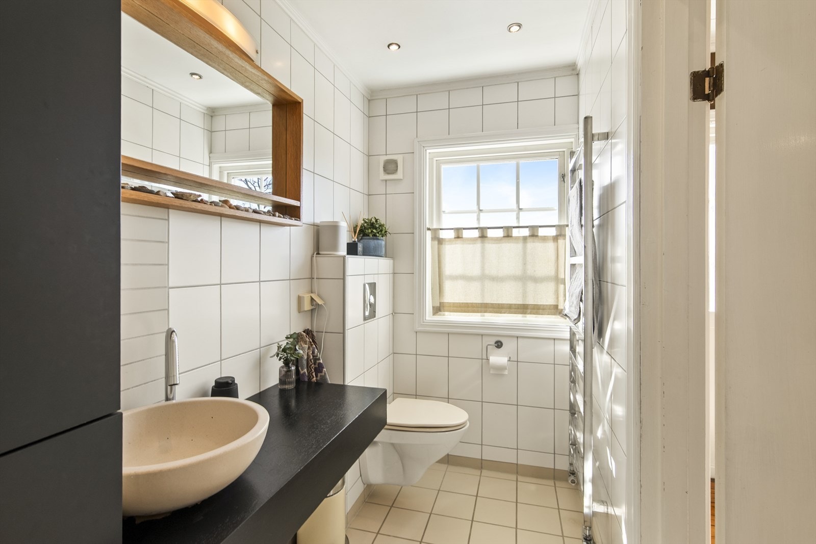 Badet har hvite fliser på veggene, downlights i himlingen og beige fliser på gulv med gulvvarme Galleribilde