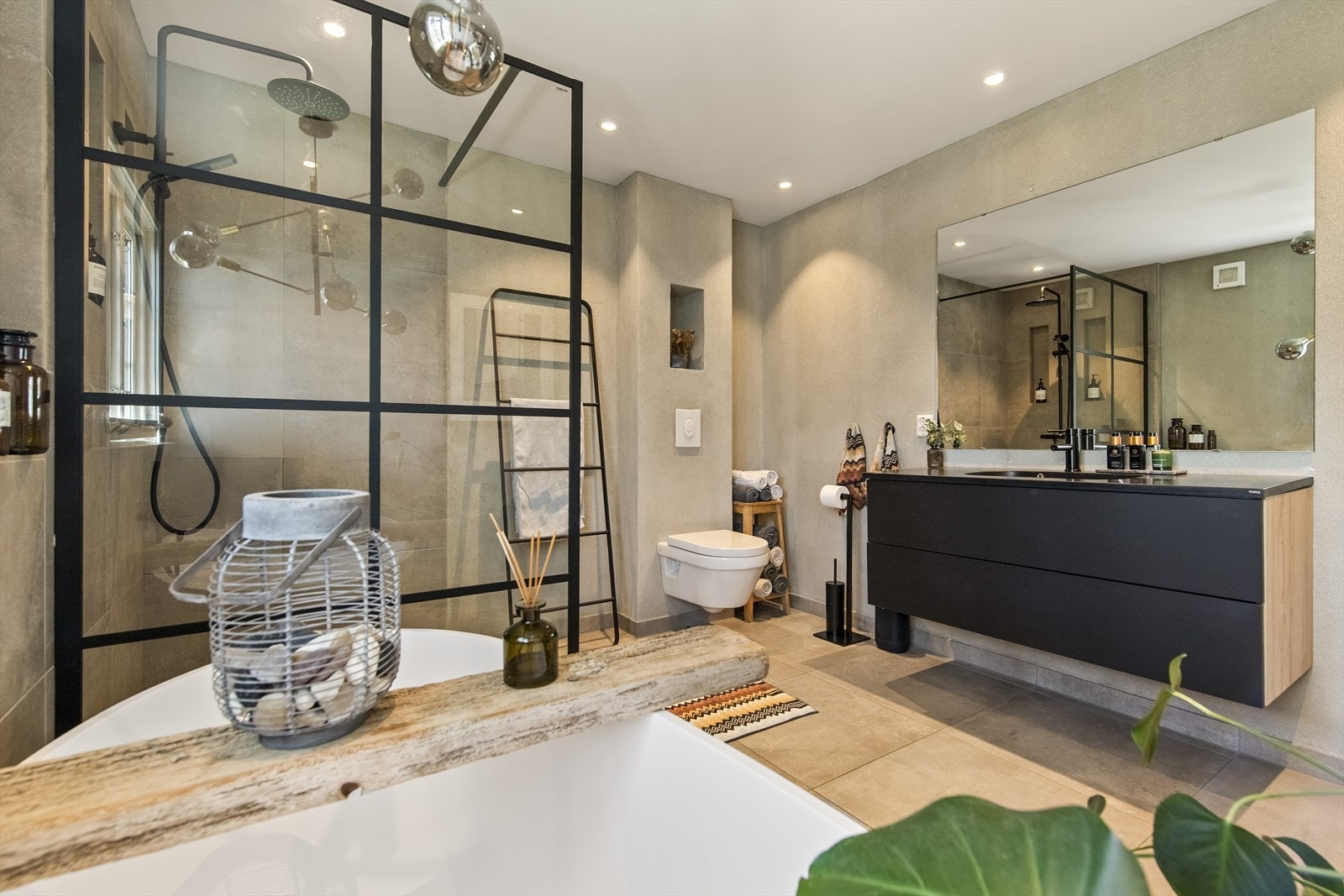 Innredningen har sorte fronter og består av en heldekkende servant på en skuffeseksjon. Videre har badet et vegghengt toalett, et moderne badekar og et dusjhjørne med regnfallsdusj bak en glassvegg. Galleribilde