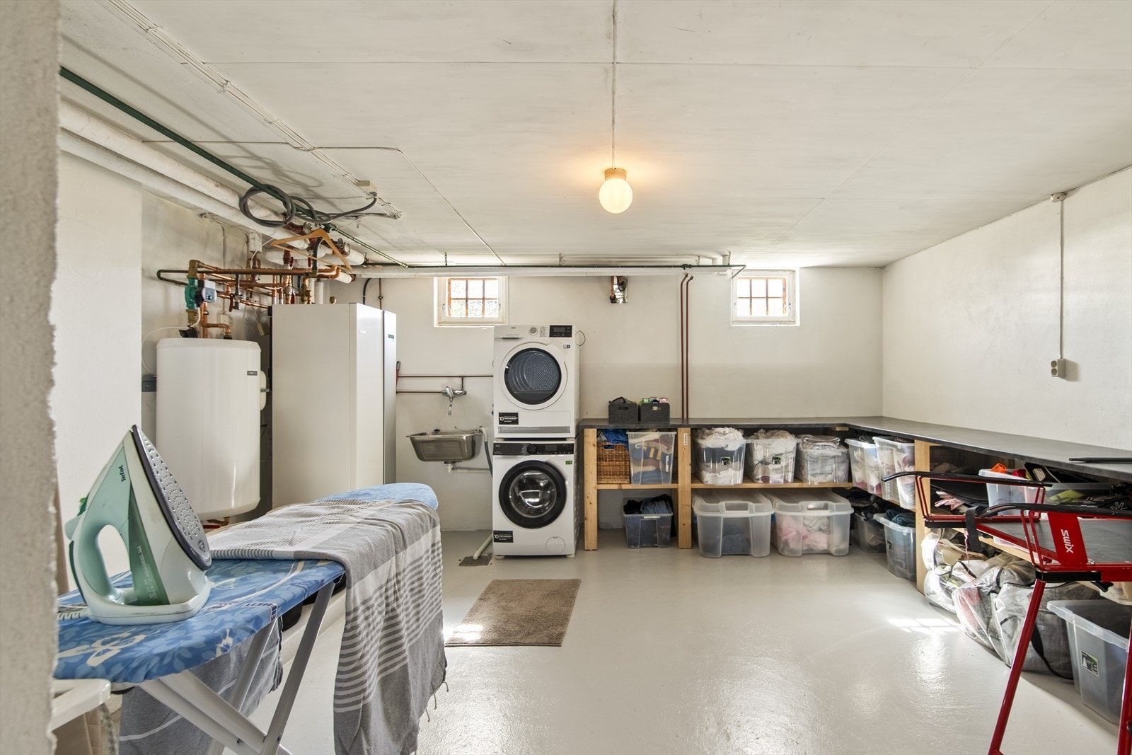 I kjelleren er det et stort og praktisk vaskerom med hvitmalte murvegger og gråmalt betonggulv med sluk. Lang benk gir gode arbeidsflater, med plass til tørkestativ og strykebrett, samt skyllekum i stål og opplegg for vaskesøyle Galleribilde