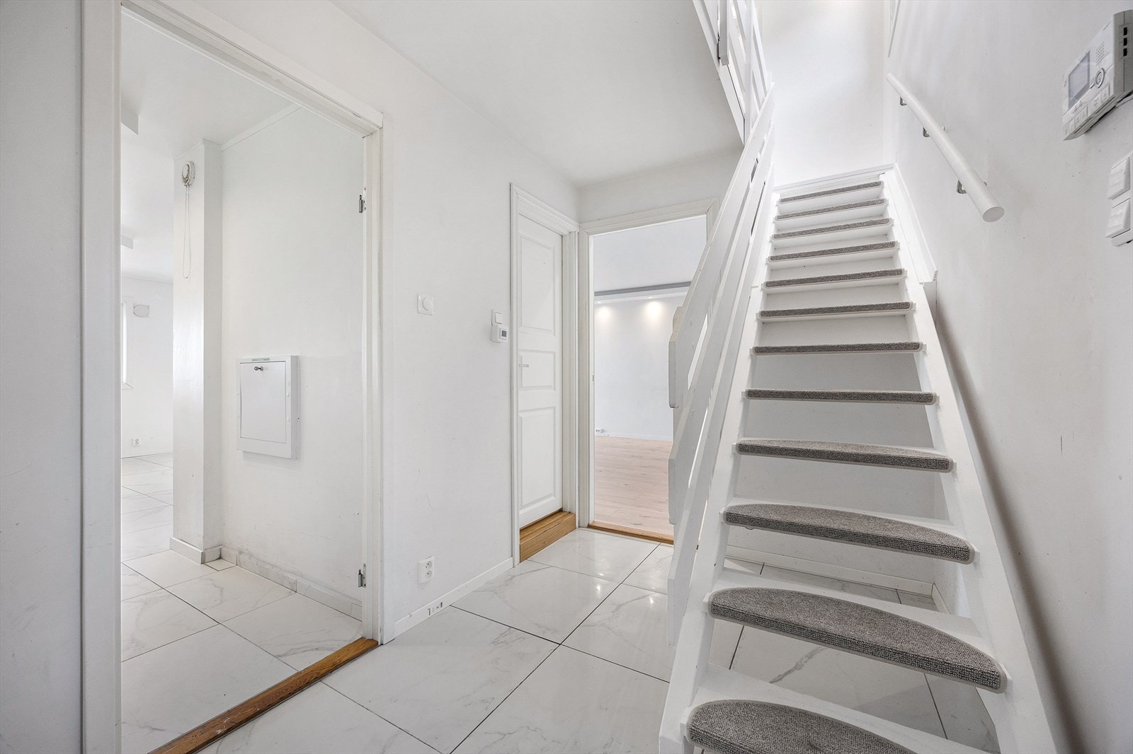 Entréen har flislagt gulv og en malt tretrapp som leder opp til leilighetens andre etasje Galleribilde