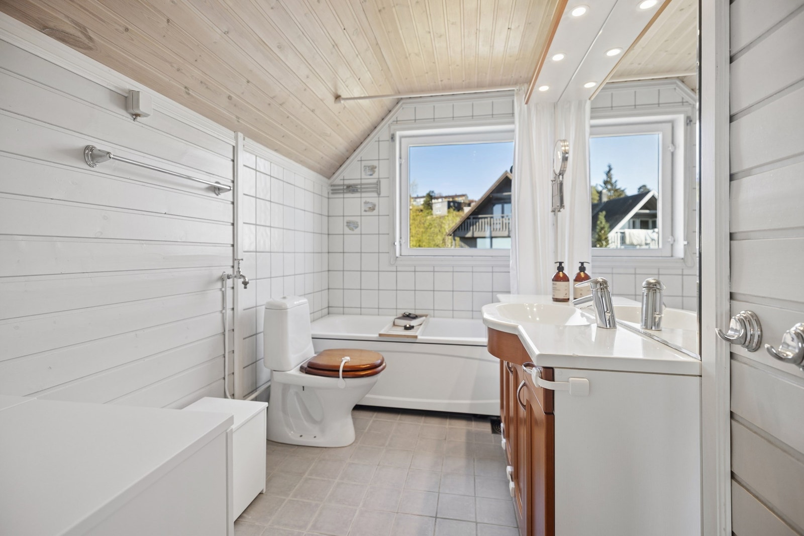 Romslig baderom med flislagt gulv og behagelig gulvvarme. Badet er innredet med badekar med veggmontert hånddusj, servantinnredning og gulvstående toalett. Galleribilde