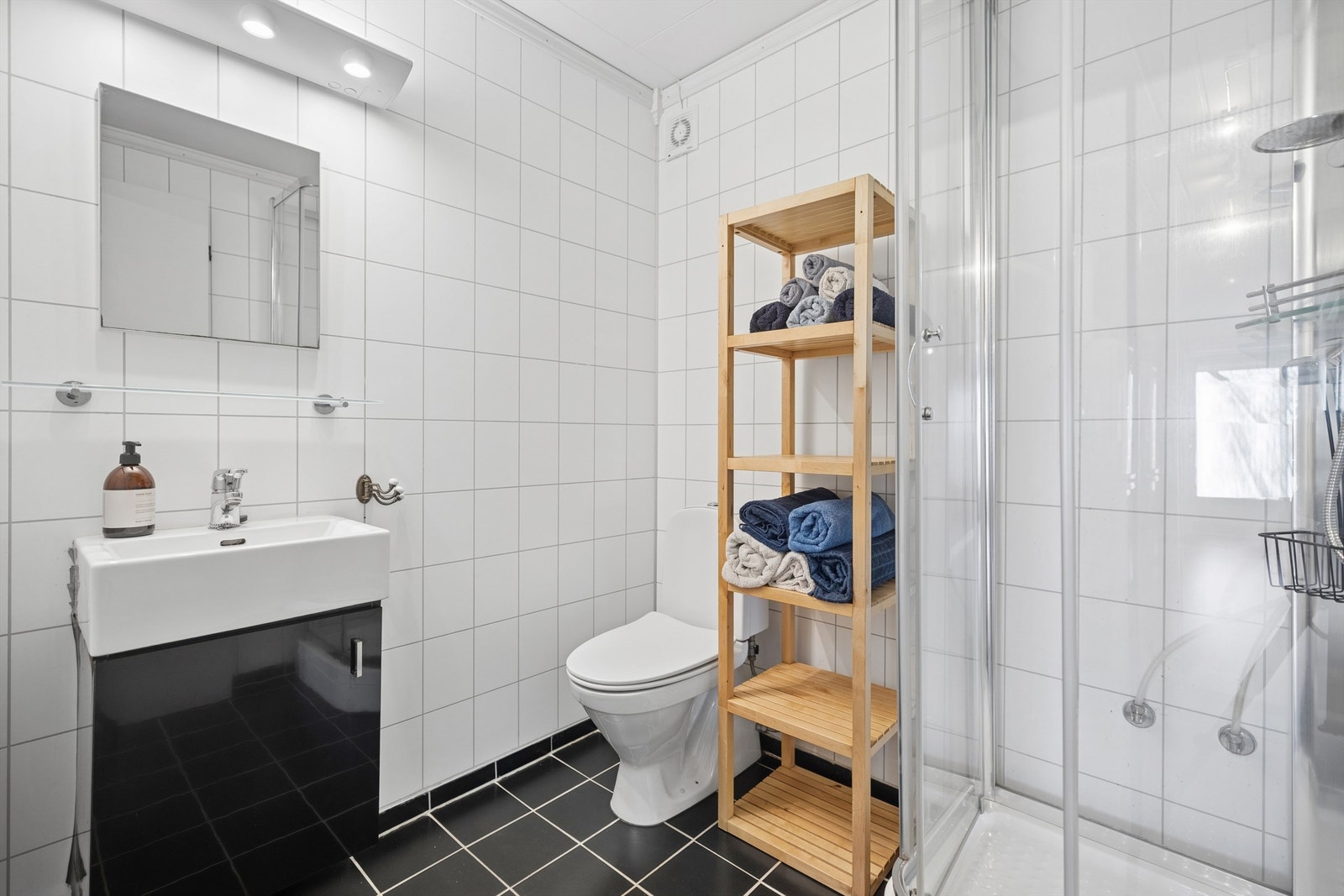 Stilrent, flislagt bad med gulvvarme. Badet er innredet med dusjkabinett, servant i innredning og gulvstående toalett. Galleribilde