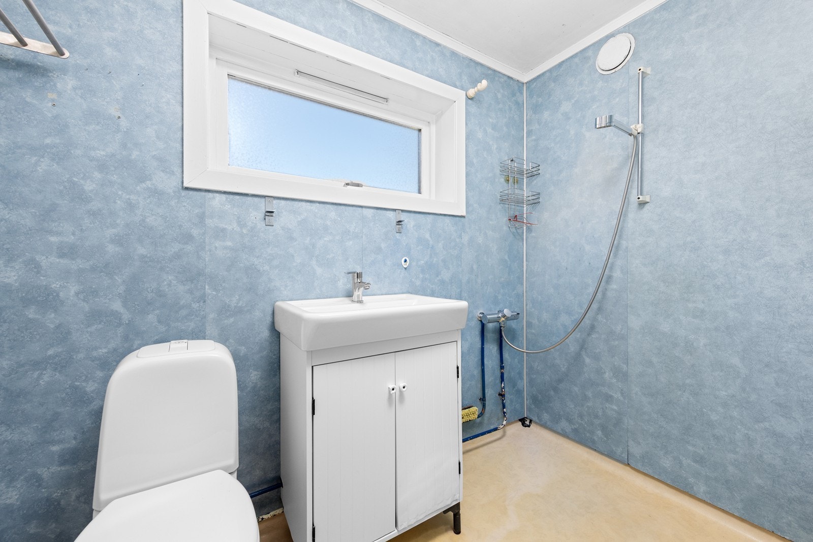 Badet er av eldre dato og har et omfattende oppgraderingsbehov. Rommet har gulvbelegg, vegger med baderomsplater og innredning med servant og toalett. Galleribilde