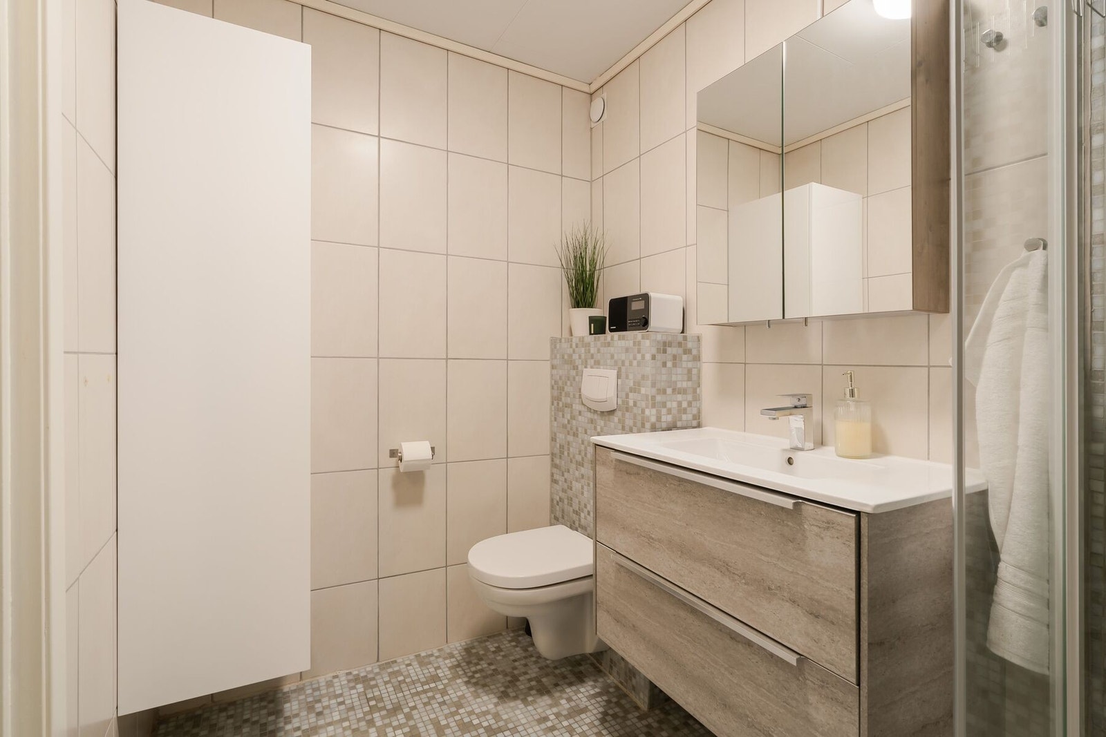 Badet er utstyrt med dusjhjørne, servant med innredning og vegghengt toalett som gir et elegant uttrykk. Galleribilde