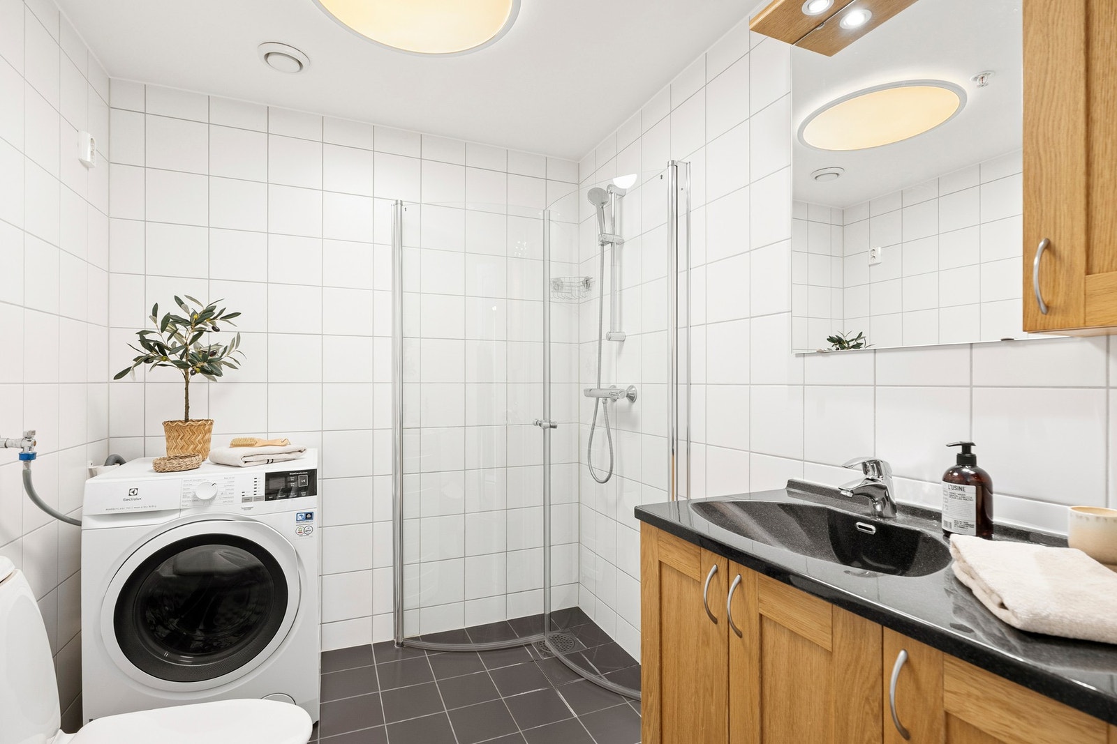 Badet fremstår lyst og innbydende, med hvite fliser på veggene og mørke fliser på gulvet som gir en fin kontrast Galleribilde