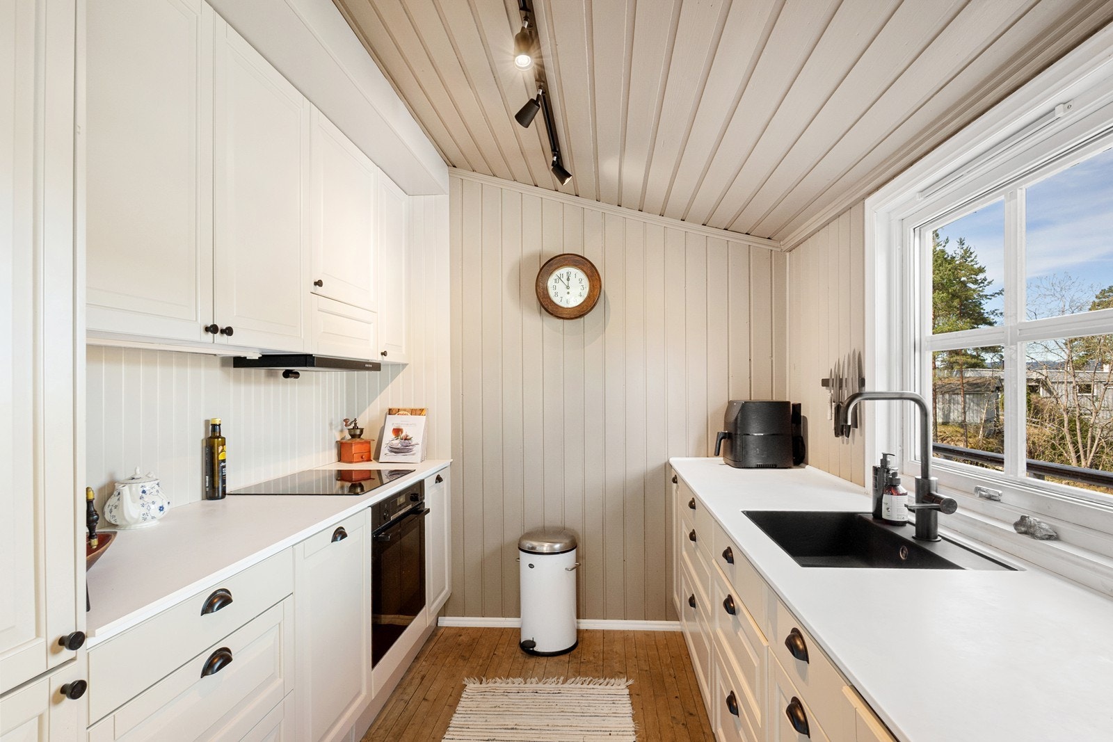 Kjøkkenet har en praktisk og stilren løsning med innredning langs to vegger. Det er utstyrt med hvite, profilerte fronter og en lys benkeplate i kompositt. Galleribilde