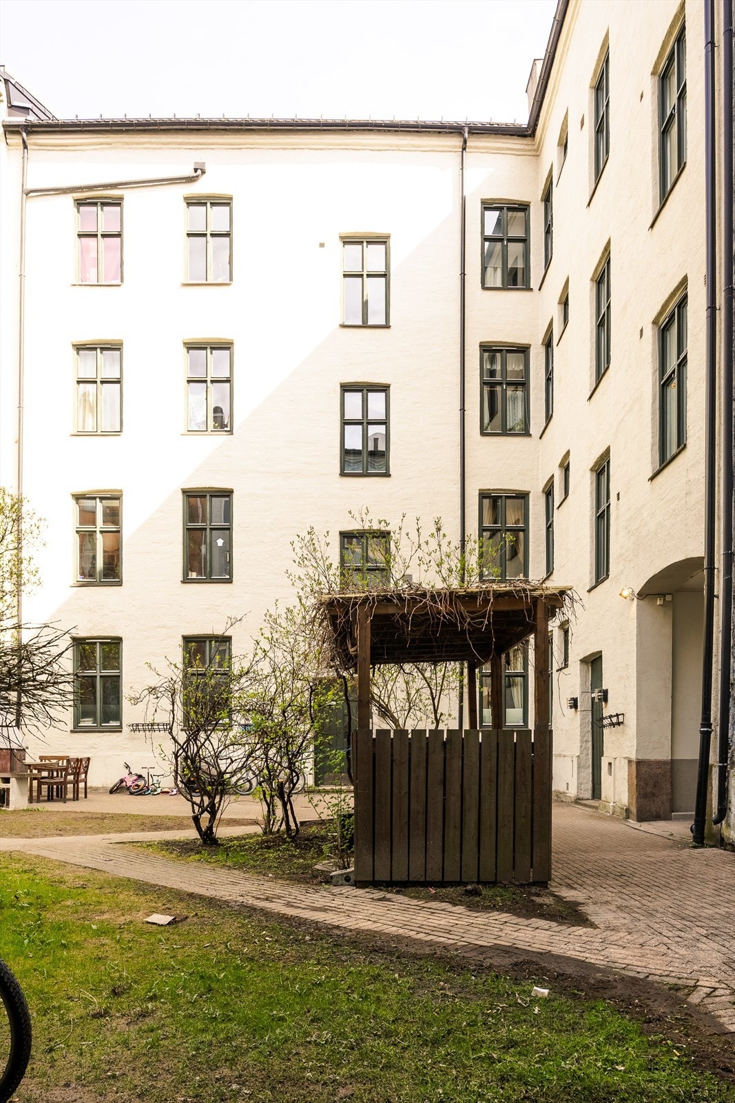 Fasade mot bakgård med lys puss, store vinduer og grønt gårdsrom Galleribilde