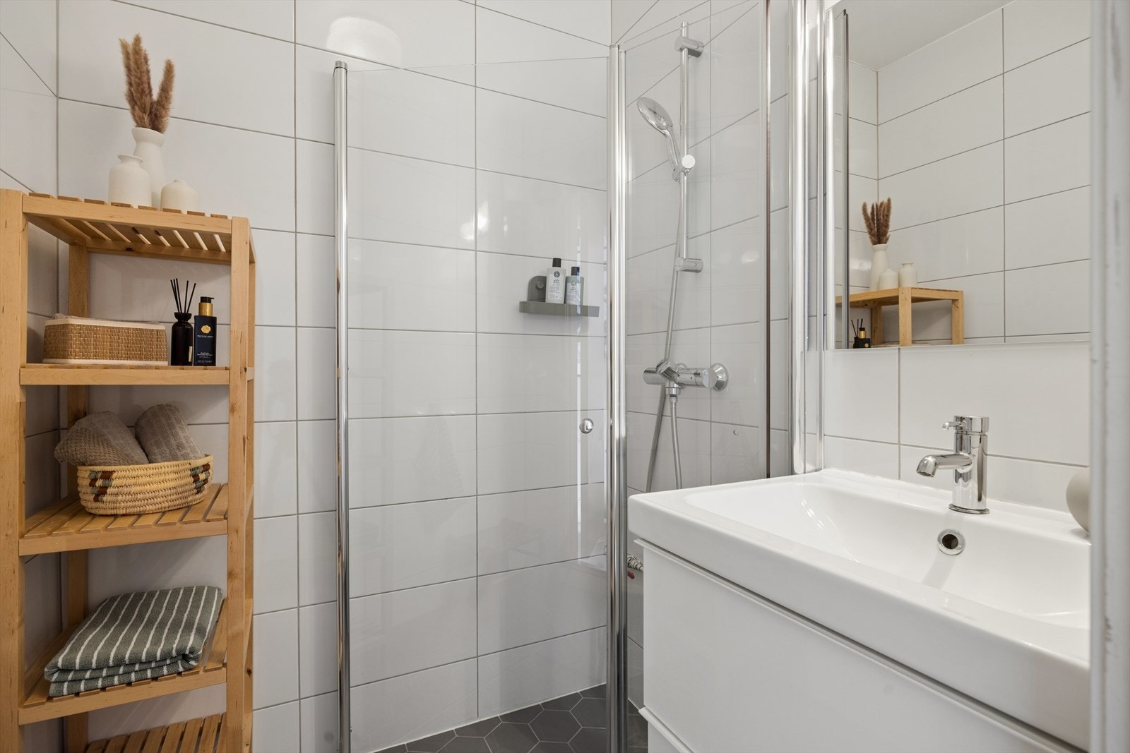 Badet har flislagte overflater, dusjhjørne og servantinnredning med speil over. Galleribilde