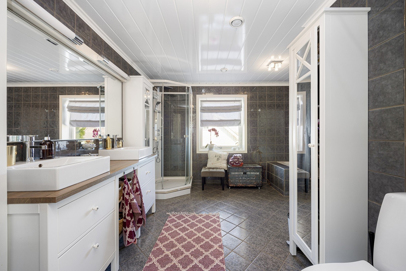 Badet i første etasje oppleves som stort, pent og velholdt, med grå fliser på veggene og matchende fliser på gulv med gulvvarme. Galleribilde