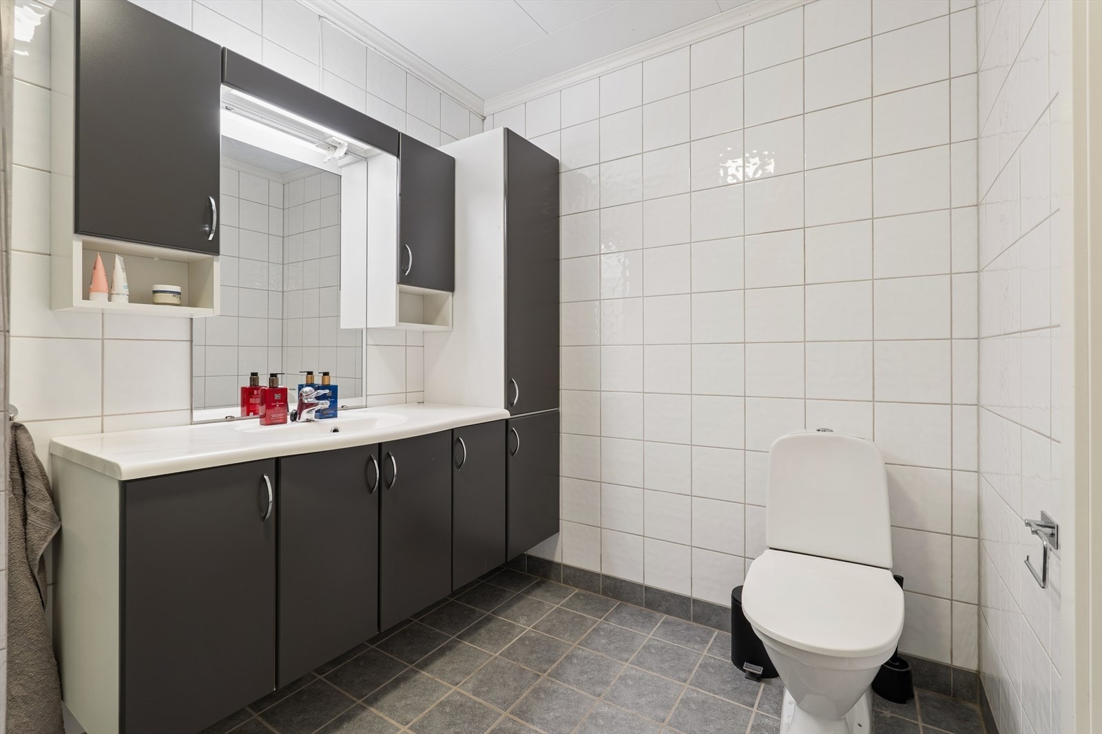 Badet inneholder mørk baderomsinnredning med nedfelt servant, toalett (nytt i 2026) og dusjvegger/hjørneløsning. Badet er utstyrt med elektriske varmekabler i gulvet som sørger for komfortabel og jevn varme. Galleribilde