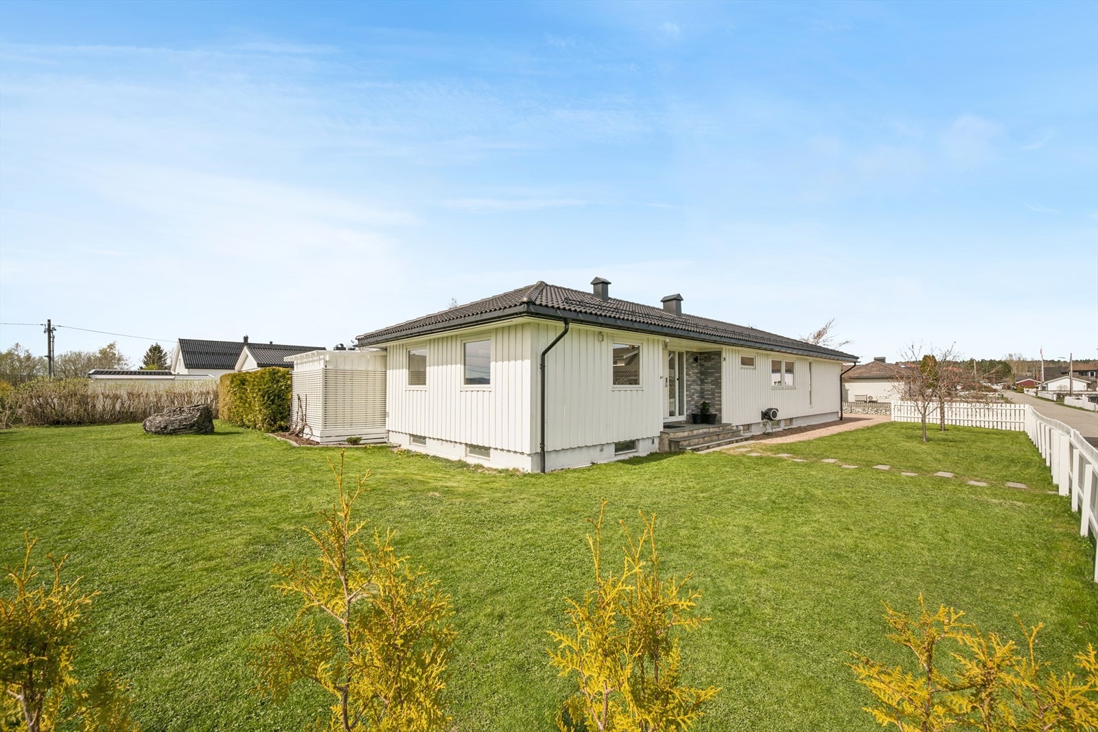 Tomten er flat og pent opparbeidet med gressplen, hekker, busker, terrasseplatting og pergola. Galleribilde