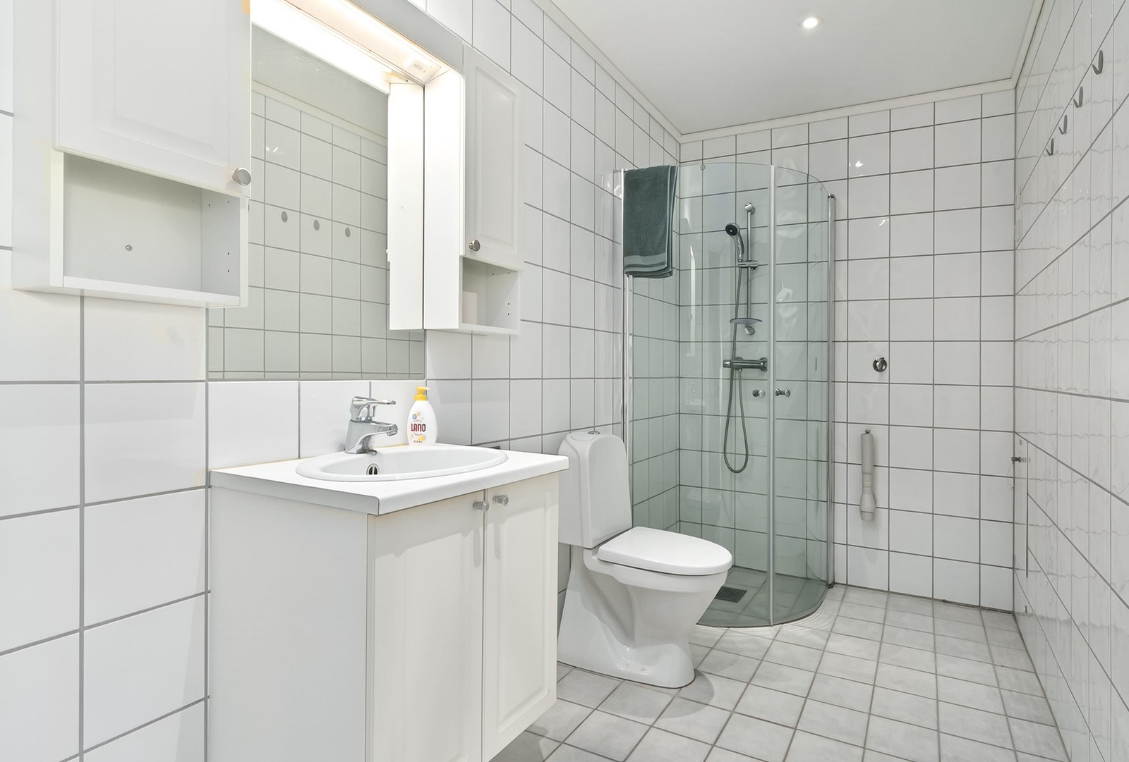 Badet har fliser på vegger og gulv, med gulvvarme. Dusjhjørne, servant innredning og opplegg for vaskemaskin. Galleribilde