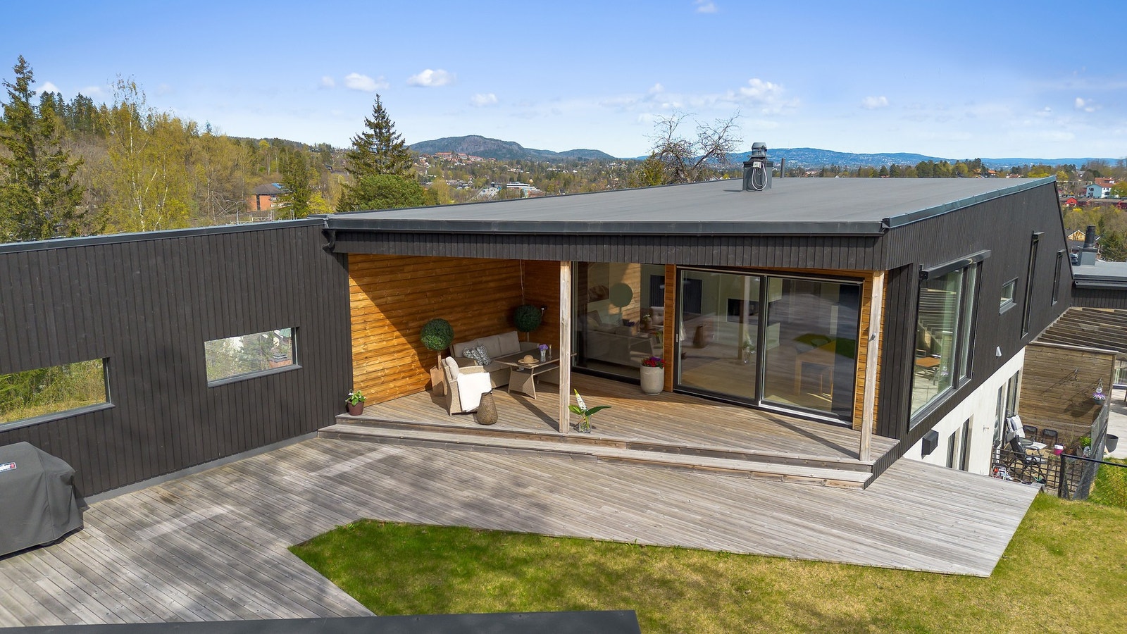 Moderne bolig med stor terrasse og hage, beliggende i et naturskjønt område med utsikt mot skog og åser Galleribilde