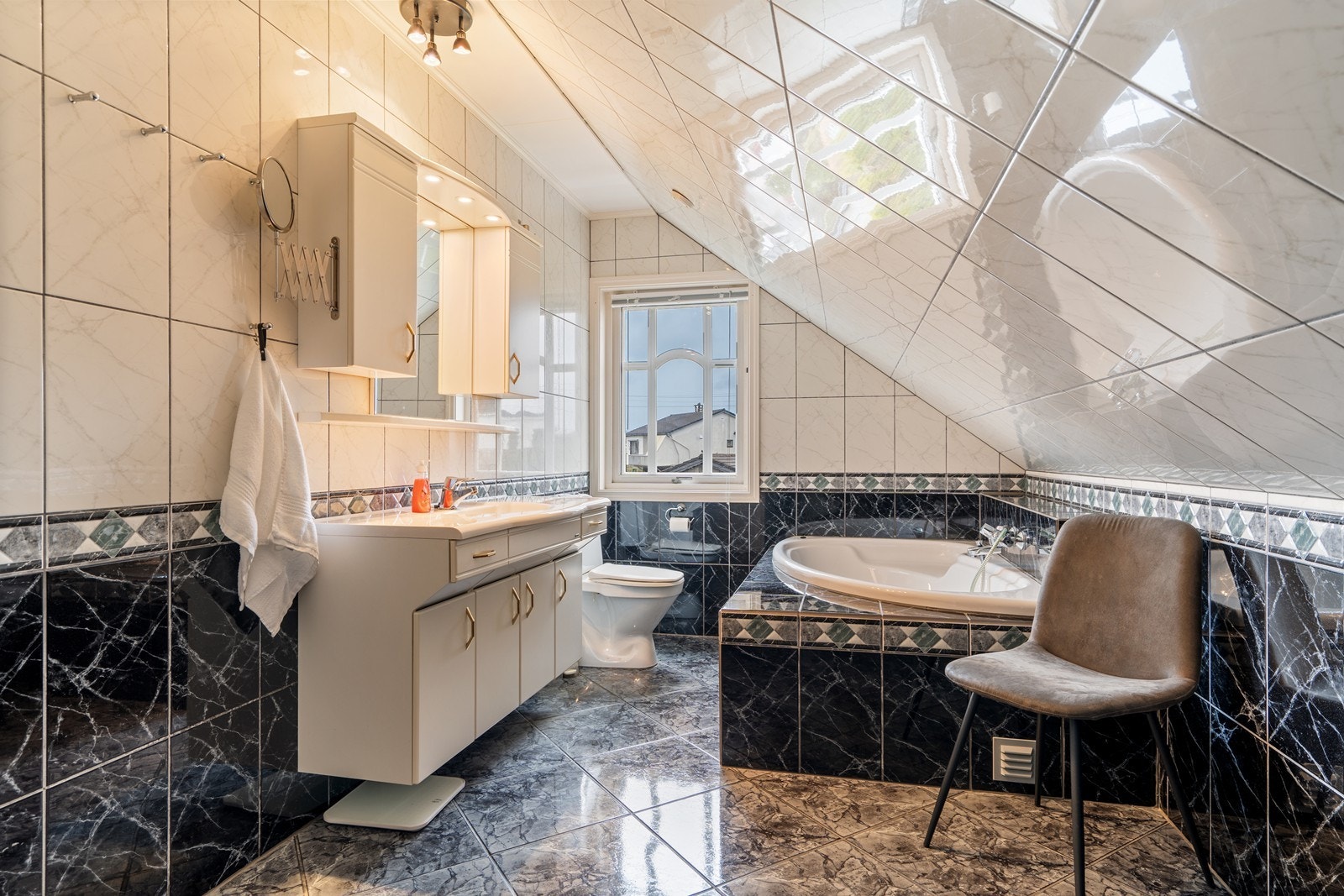 Pent, helfliset bad på loftet med varmekabler i gulvet - badet er innredet med hvit baderomsinnredning, gulvmontert toalett og innebygd badekar Galleribilde