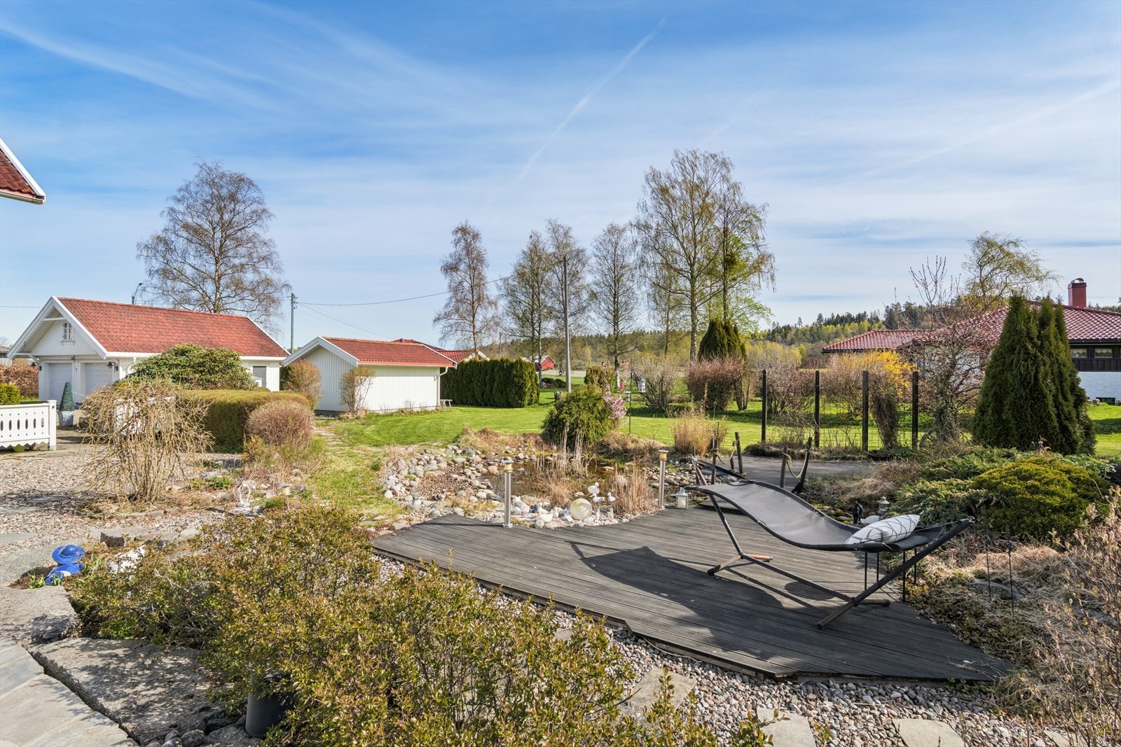Flere soner i hagen, inkludert en platting ved dammen, inviterer til avslapning og rekreasjon. Galleribilde