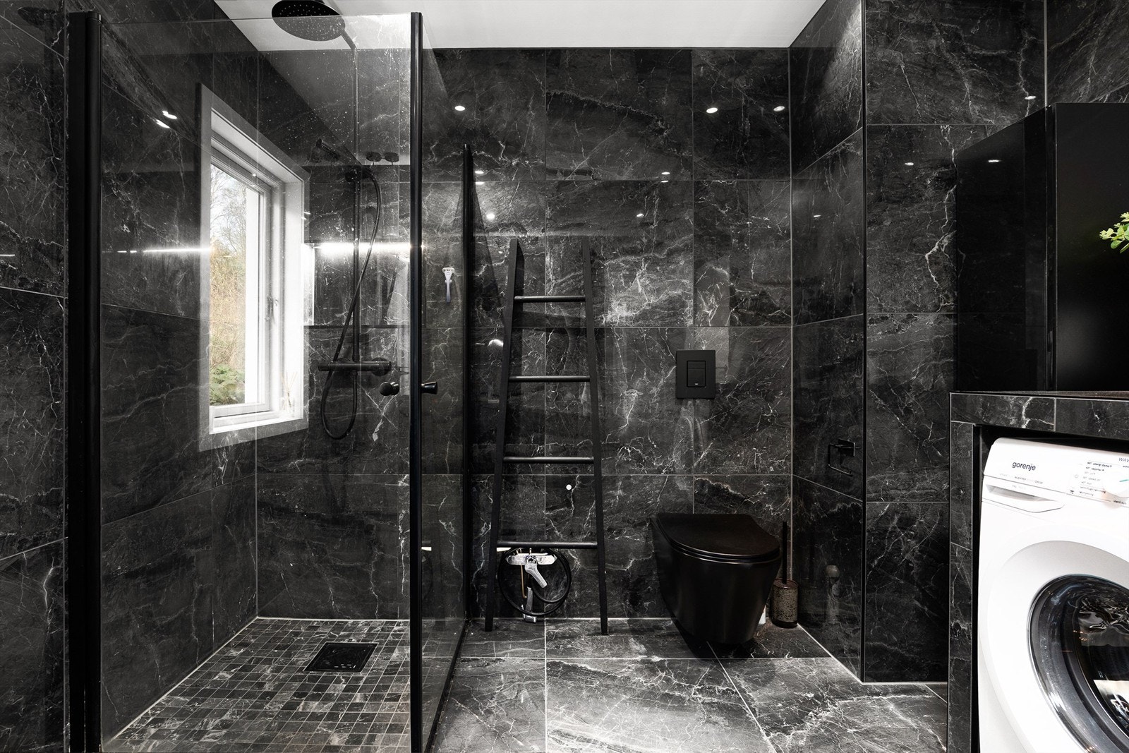 Mørke, marmorerte storformat fliser på vegger og gulvet utenom dusjsonen gir badet helhet. Galleribilde