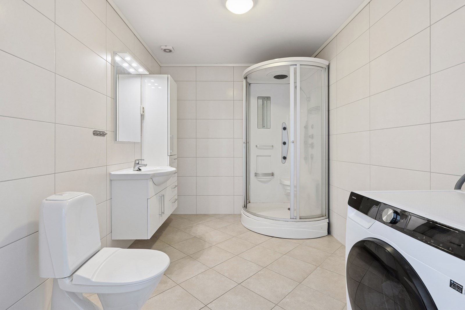 Flislagt baderom i tidløse fargekombinasjoner! Badet er utstyrt med dusjkabinett, toalett, baderomsinnredning og opplegg til vaskemaskin/tørketrommel Galleribilde