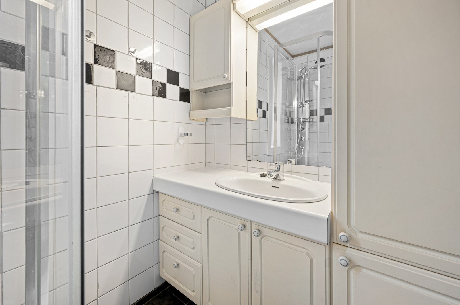 Badet er innredet med servantinnredning, speil, overskap, dusjkabinett, varmtvannstank og opplegg for vaskemaskin. Galleribilde