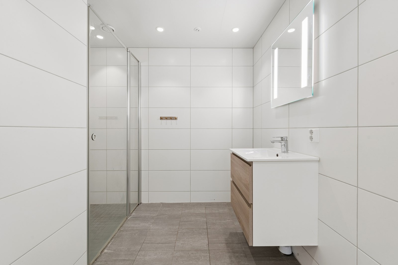 Badet er helfliset og med varme i gulvet. Innredningen består av heldekkende servant med to skuffer, speil med integrert belysning og vegghengt toalett. Galleribilde