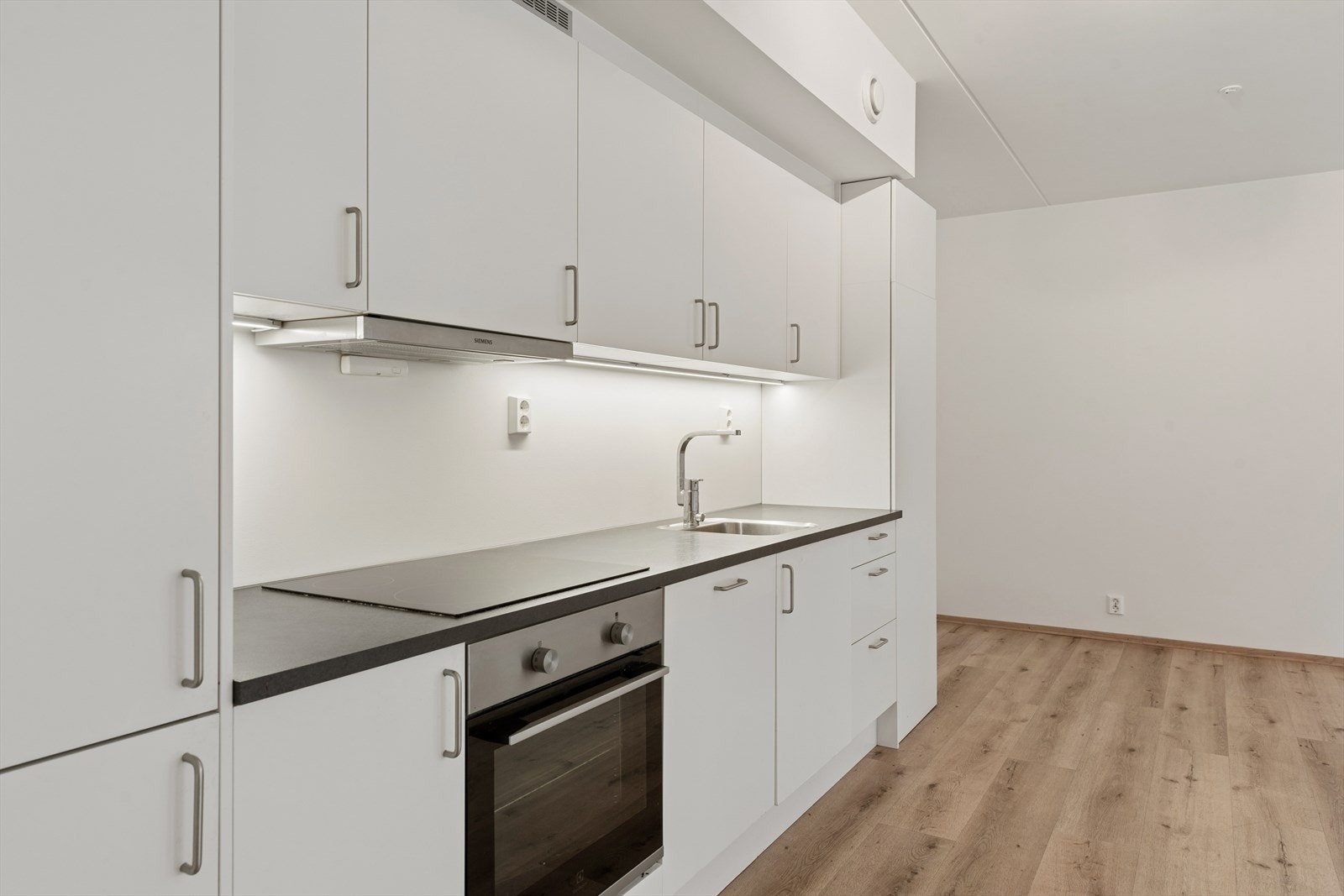 Laminat benkeplate med planlimt kum i rustfritt stål. Hvitevarer i form av integrert induksjonstopp, stekeovn, oppvaskmaskin og kjøl/frys. Galleribilde