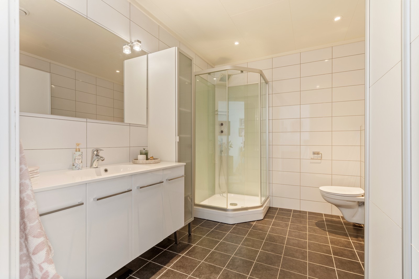 Badet er av god størrelse og er innredet med baderomsmøbel med heldekkende servant, veggmontert toalett og dusjkabinett. Galleribilde