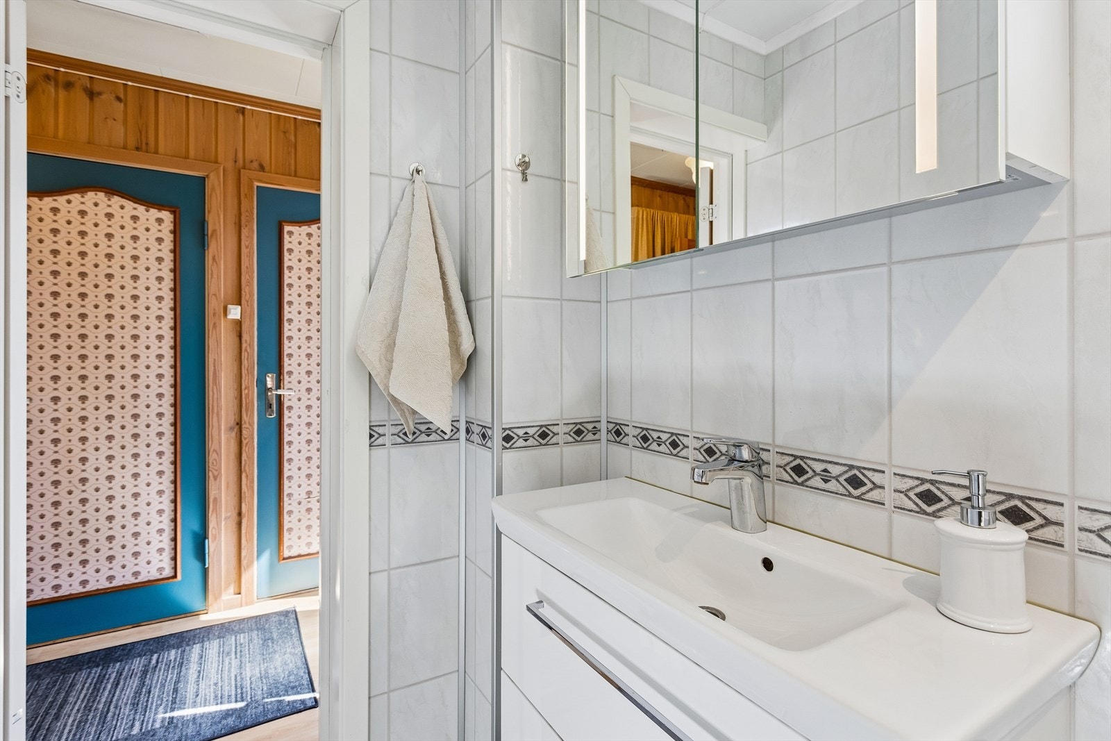 Moderne baderomsinnredning med heldekkende servant og overskap skap med speilfronter og belysning. Galleribilde
