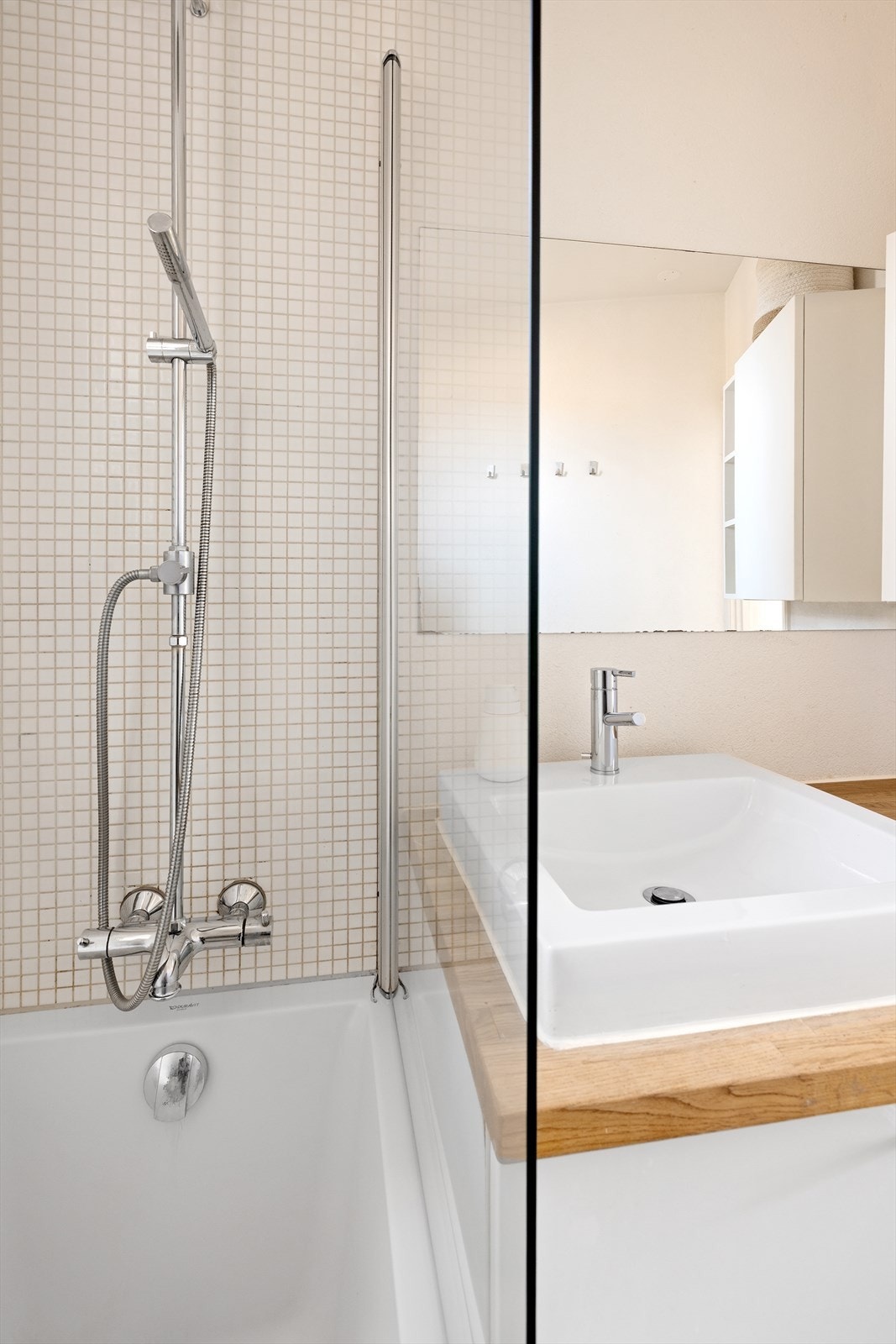Badet har dusjløsning over badekar og lyse flislagte overflater Galleribilde