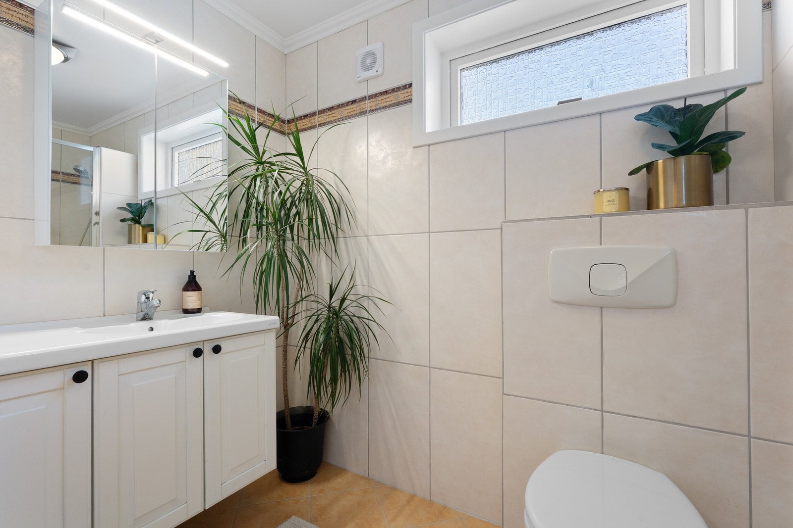 Badet inneholder vegghengt toalett, helstøpt servant og skap under servant med profilerte fronter, samt dusjdør i klart glass. Galleribilde