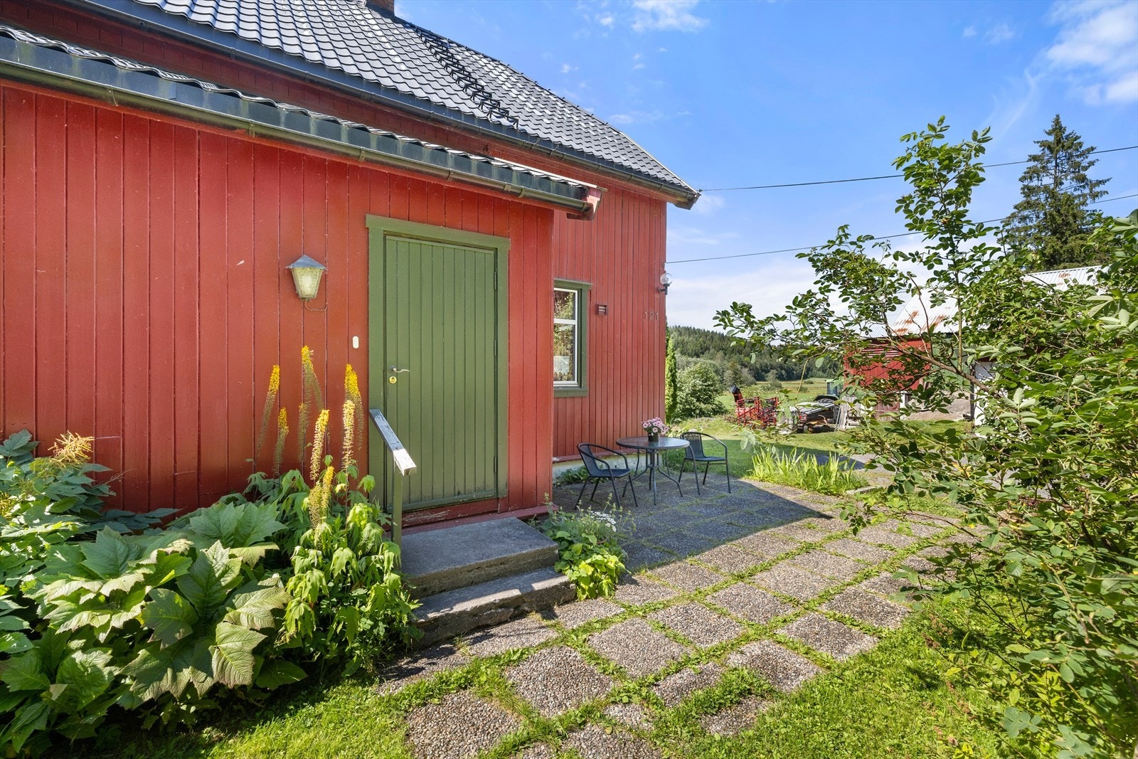 Hyggelig inngangsparti med belegningsstein, omkranset av blomster og frodig beplantning. Galleribilde
