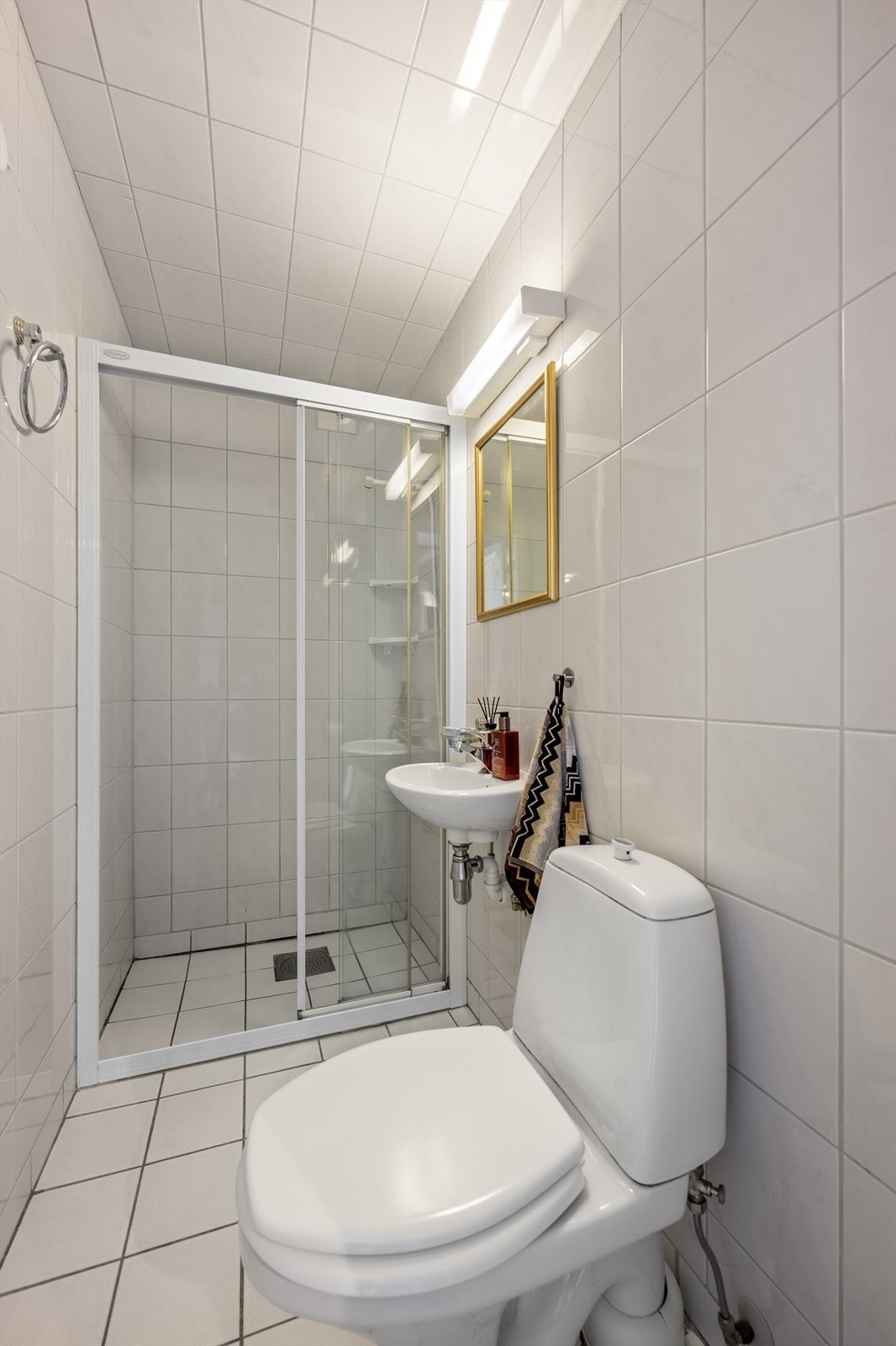 Leilighetens første bad er innredet med fliser på gulv og vegger. Badet er utstyrt med servant, gulvmontert toalett og dusjsone med skyvedører. Det anbefales å installere dusjkabinett grunnet begrenset membran. Galleribilde