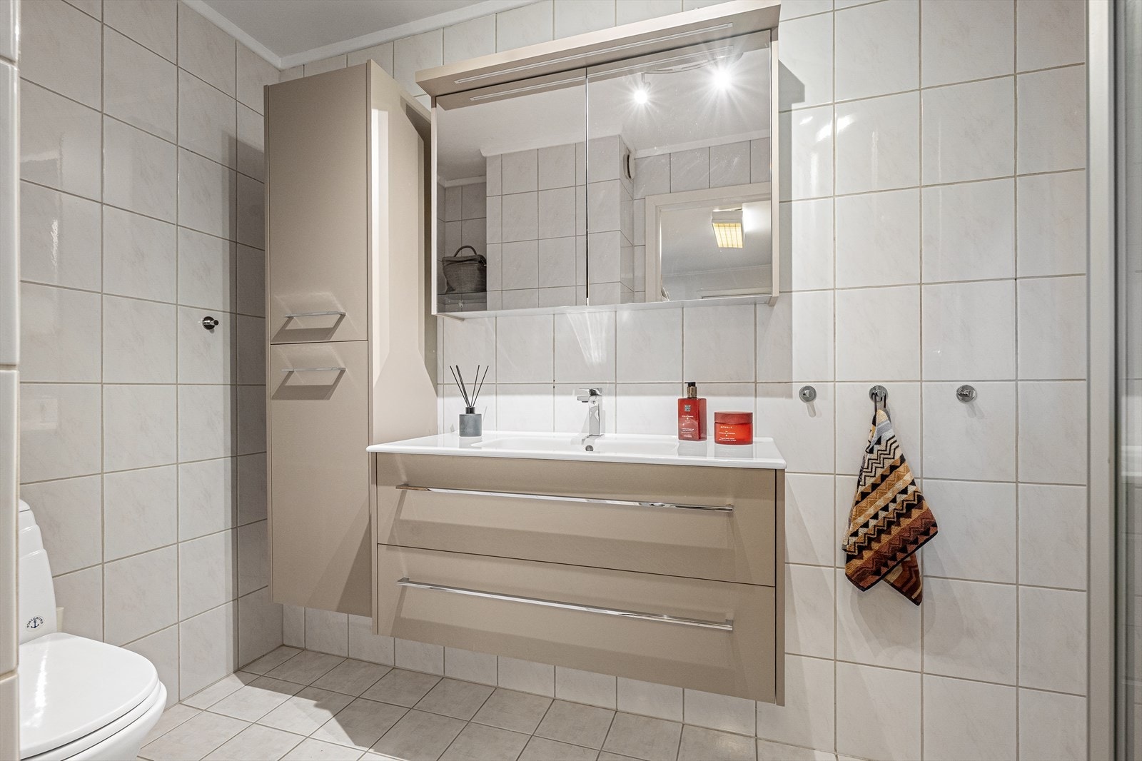 Leilighetens andre bad har fliser på gulv og vegger. Badet er har servantskap med nedfelt servant, veggskap med speildører og belysning over, samt gulvmontert toalett. Galleribilde