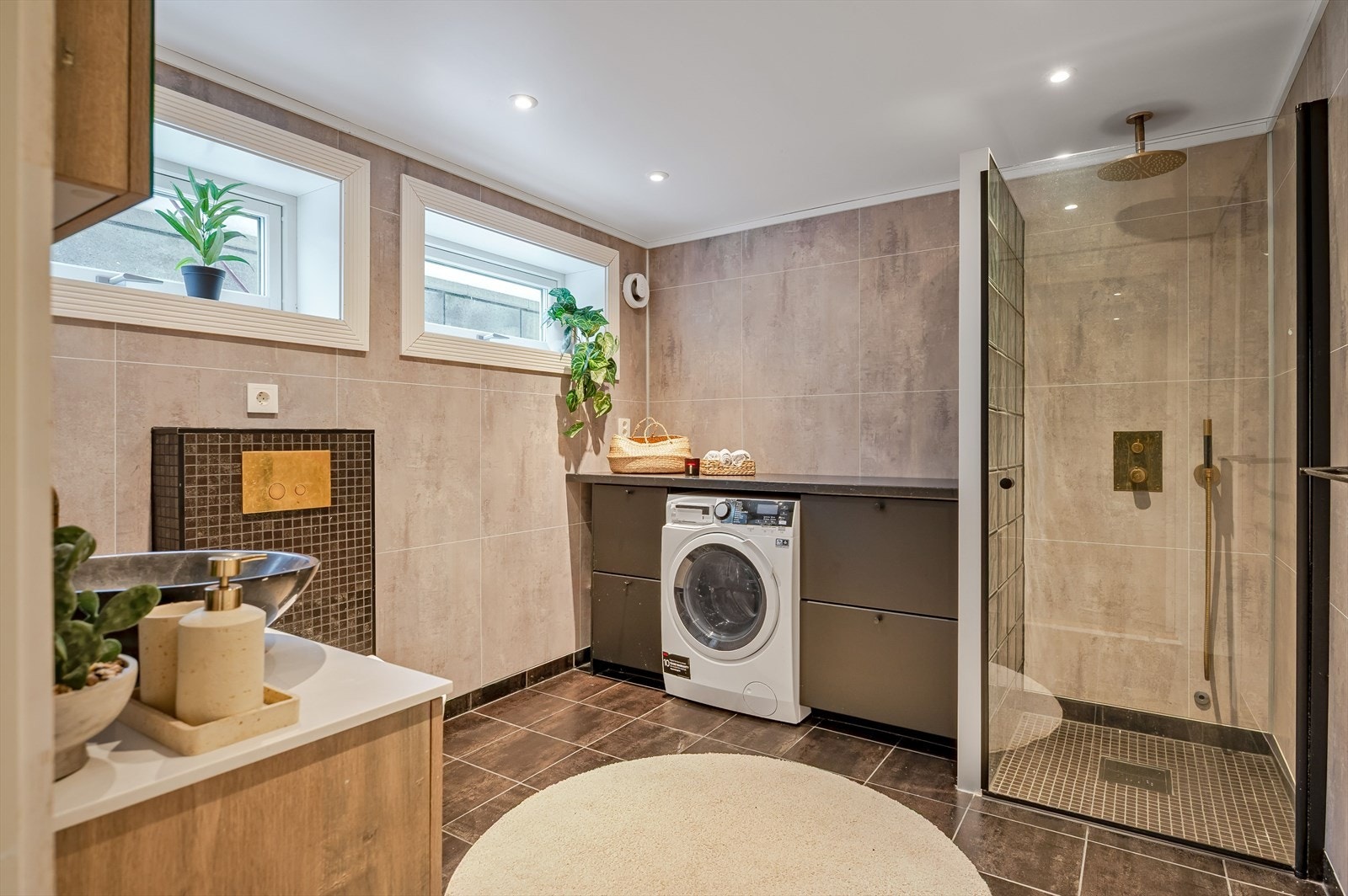 Badet i underetasjen har flislagt gulv og baderomsplater på veggene, opplegg for vaskemaskin og dusj med glassvegg. Galleribilde