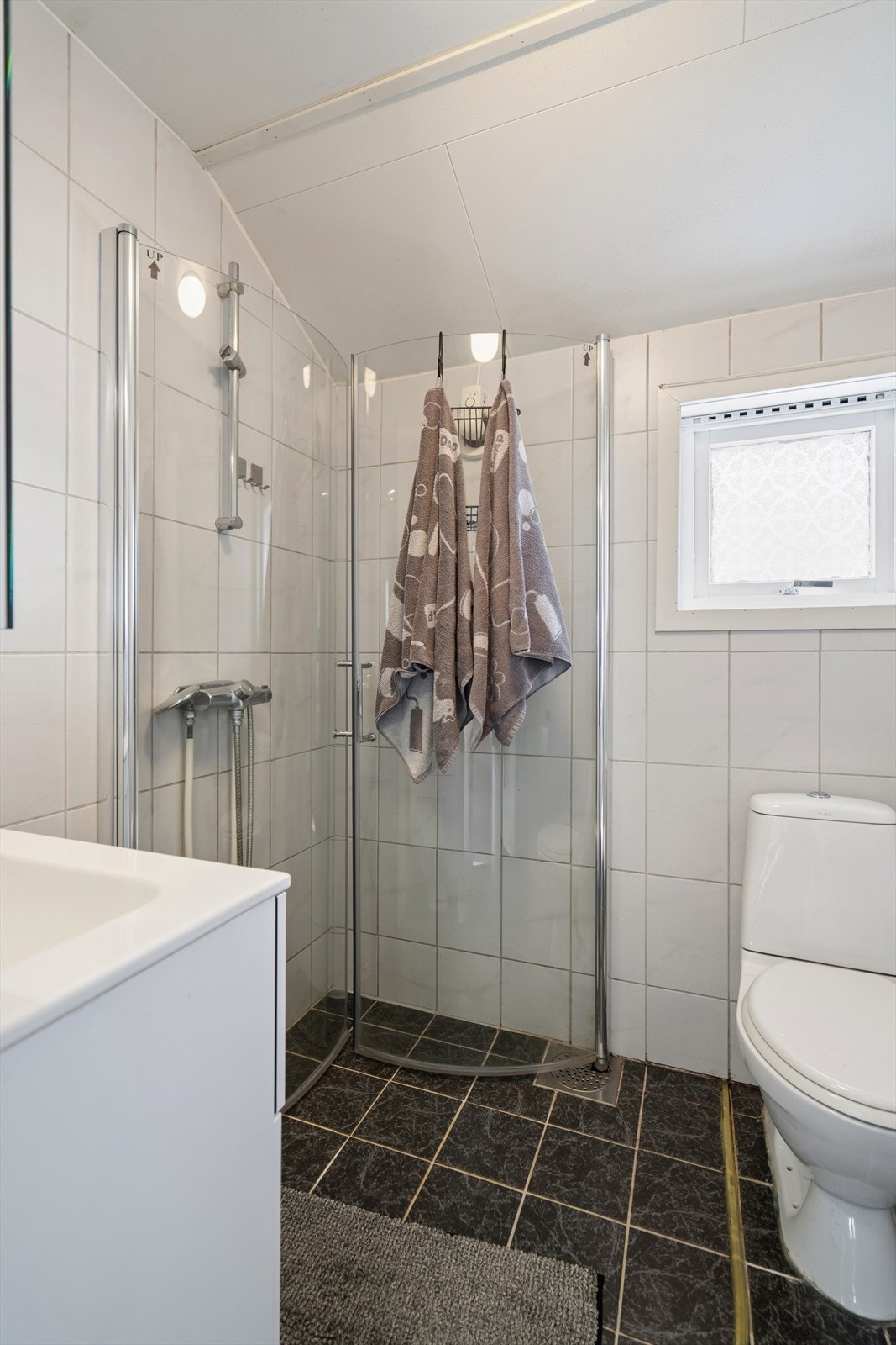 Rommet er innredet med dusjvegger, servant og gulvmontert toalett. Badet ble oppusset i 2000. Galleribilde