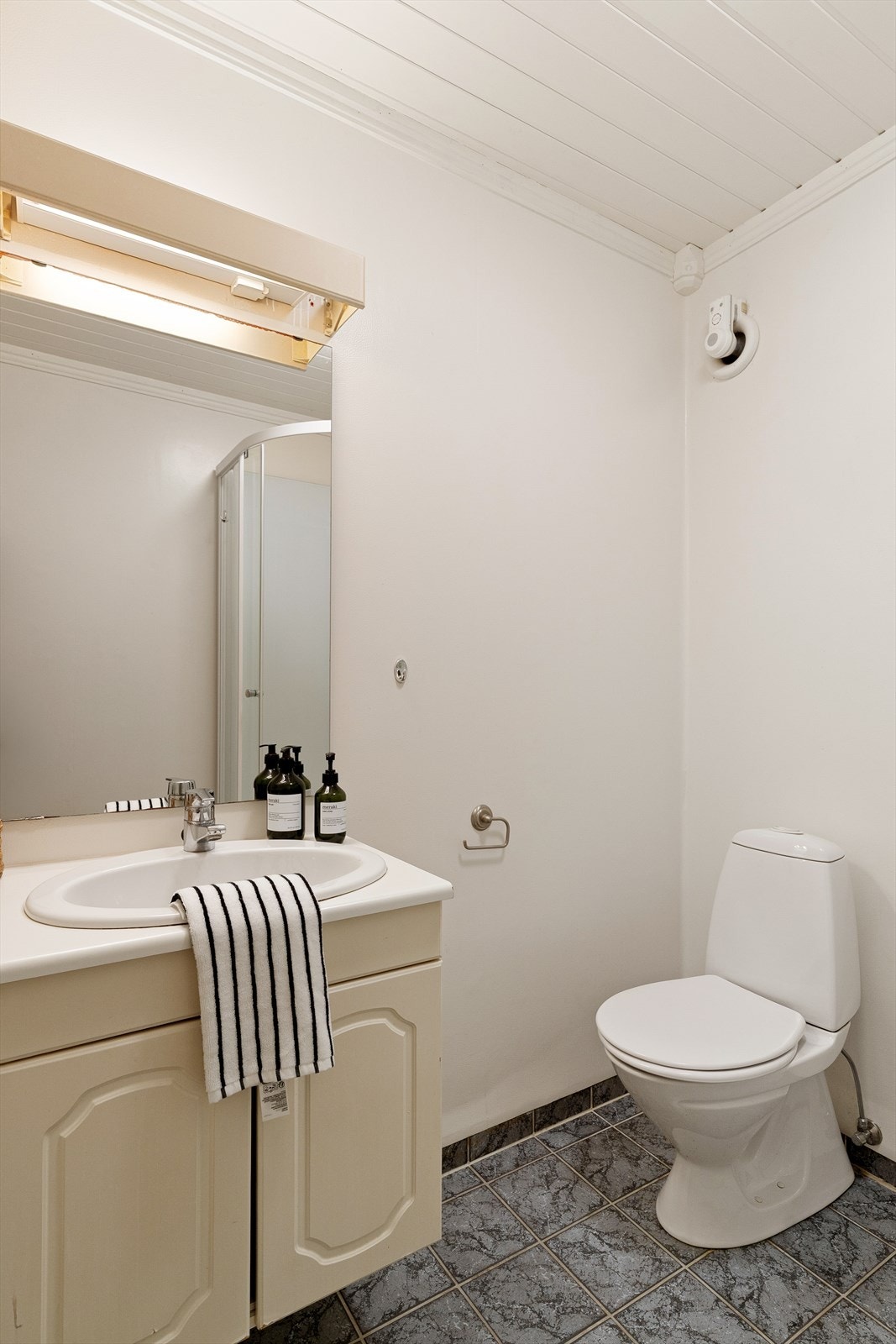 Badet er innredet med flislagt gulv, servant og dusjkabinett. Galleribilde
