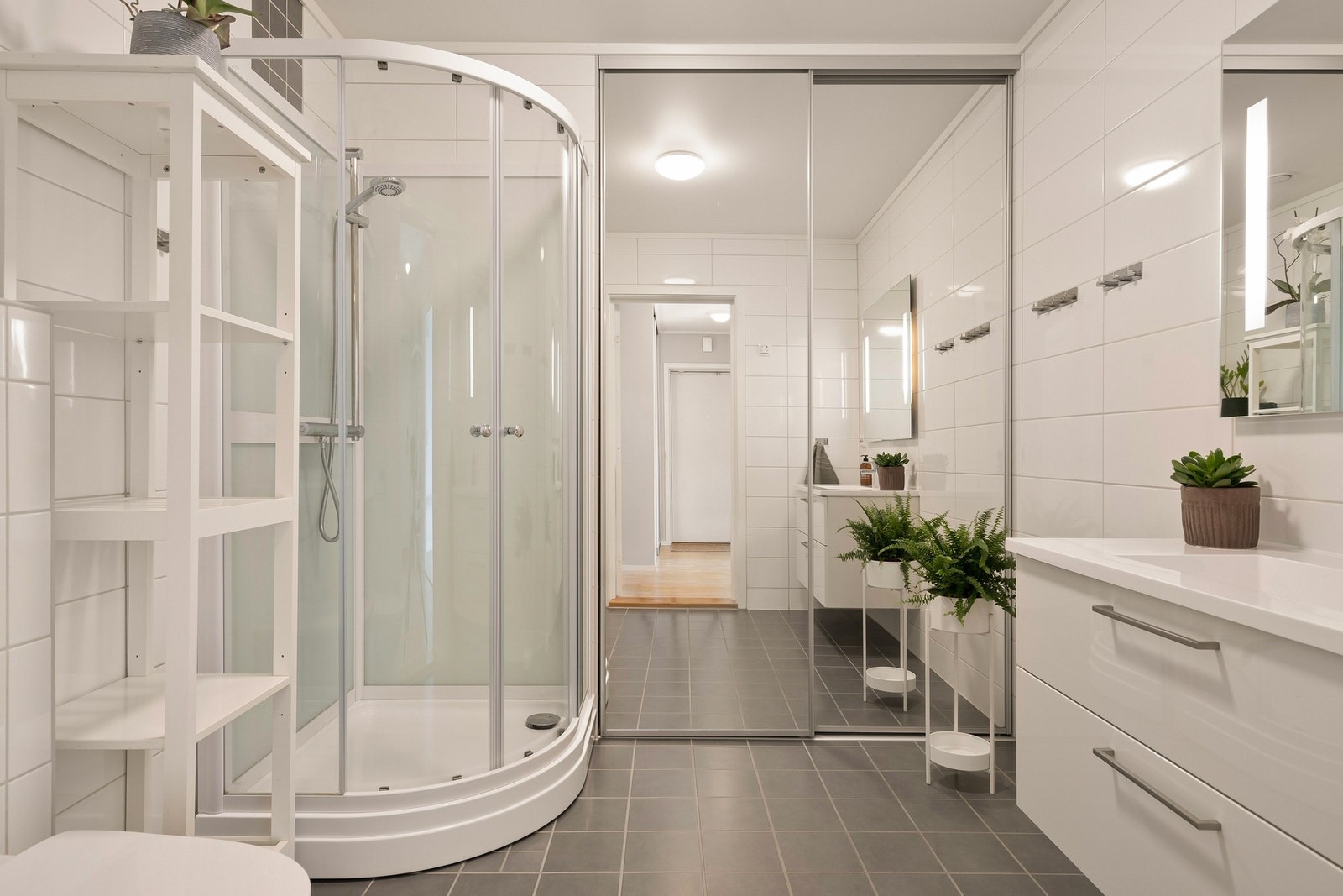 Flislagt bad med innredning med nedfelt servant, veggmontert toalett, dusjkabinett og opplegg for vaskemaskin. Galleribilde